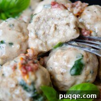 Crave-Worthy Gluten-Free Chicken Meatballs 9 A perfectly cooked gluten-free chicken meatball cut in half, showcasing its moist interior, with a fork resting beside it, all coated in a rich, creamy sun-dried tomato sauce.
