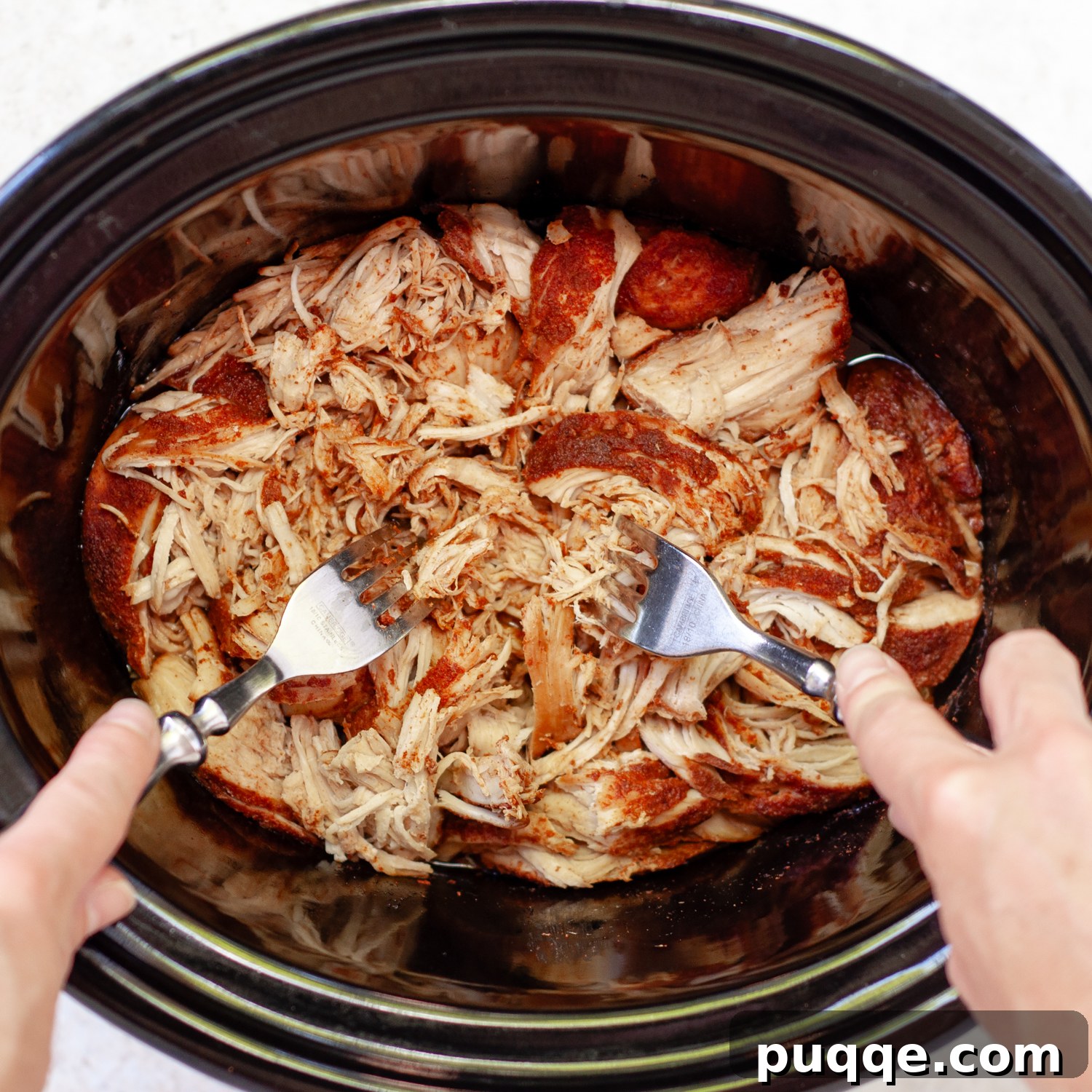 Quick Prep Slow Cooker BBQ Pulled Chicken 4 Two forks actively shredding tender chicken in a crock pot, surrounded by cooking liquid.