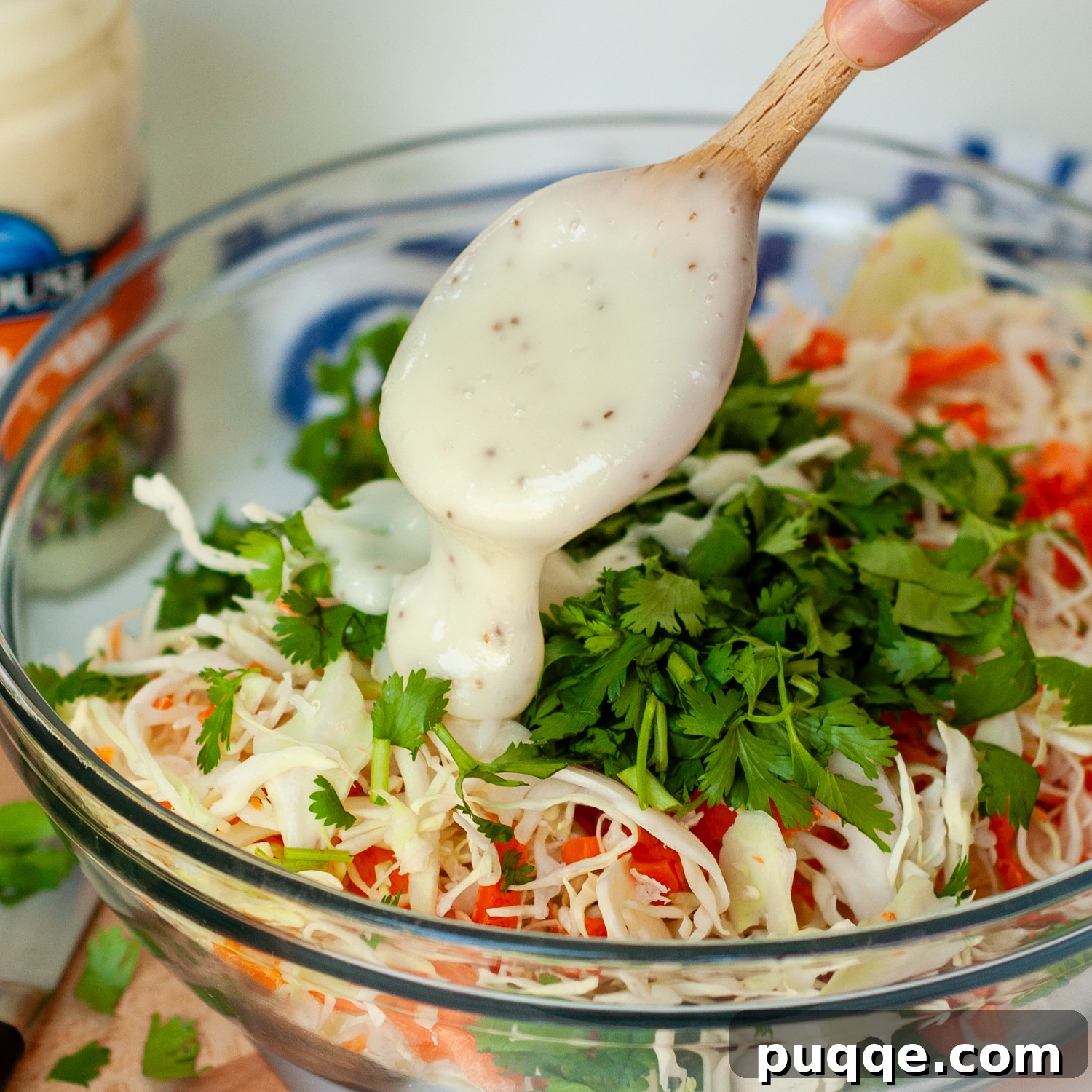 Quick Prep Slow Cooker BBQ Pulled Chicken 5 Coleslaw dressing being stirred into a bowl of shredded cabbage and carrots.