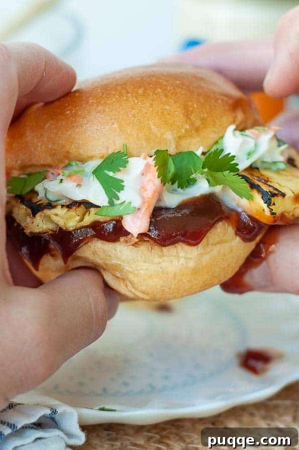 Quick Prep Slow Cooker BBQ Pulled Chicken 6 Two hands holding up a BBQ pulled chicken sandwich, showcasing the generous filling of pulled chicken, coleslaw, and grilled pineapple.