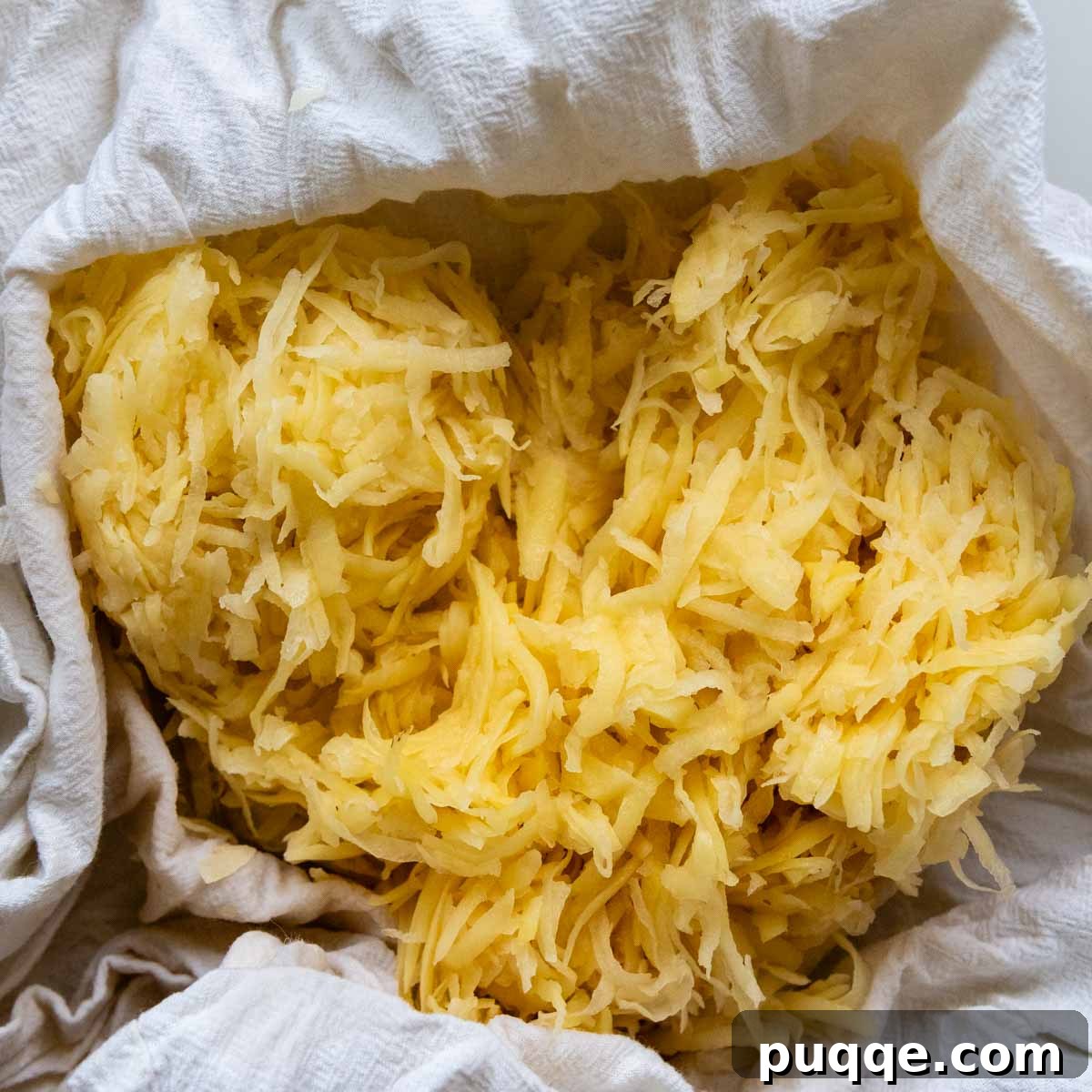 Effortless Crispy Potato Rösti 3 Close-up view of freshly grated raw Yukon Gold potatoes bundled in a white flour sack towel, ready for moisture removal.