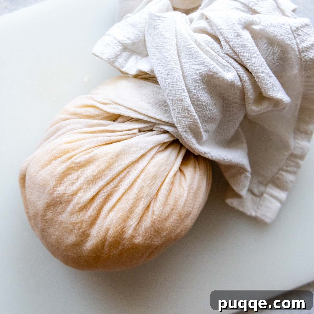 Effortless Crispy Potato Rösti 4 Hands squeezing grated potatoes wrapped in a white kitchen towel, demonstrating the process of removing excess moisture.