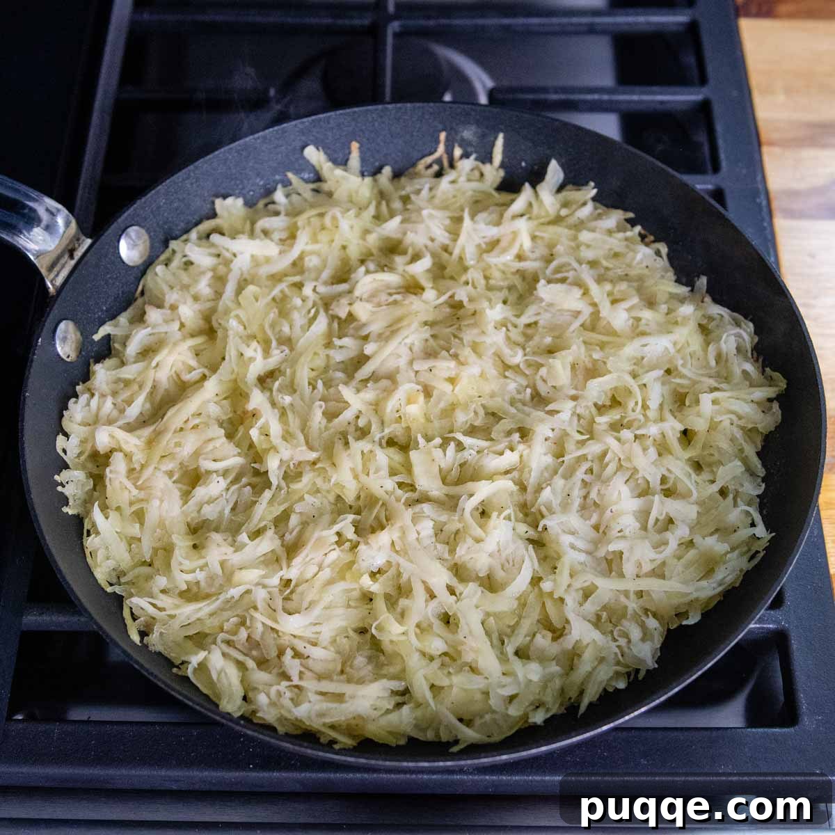 Effortless Crispy Potato Rösti 5 Grated potatoes cooking in a non-stick skillet, forming the base of a Swiss potato rosti.