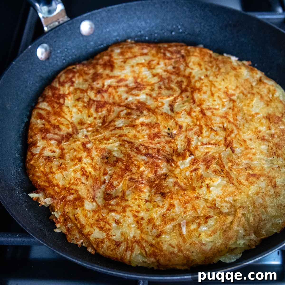 Effortless Crispy Potato Rösti 7 Overhead shot of a perfectly round, golden-brown potato rosti sizzling in a skillet, indicating it's nearly ready.