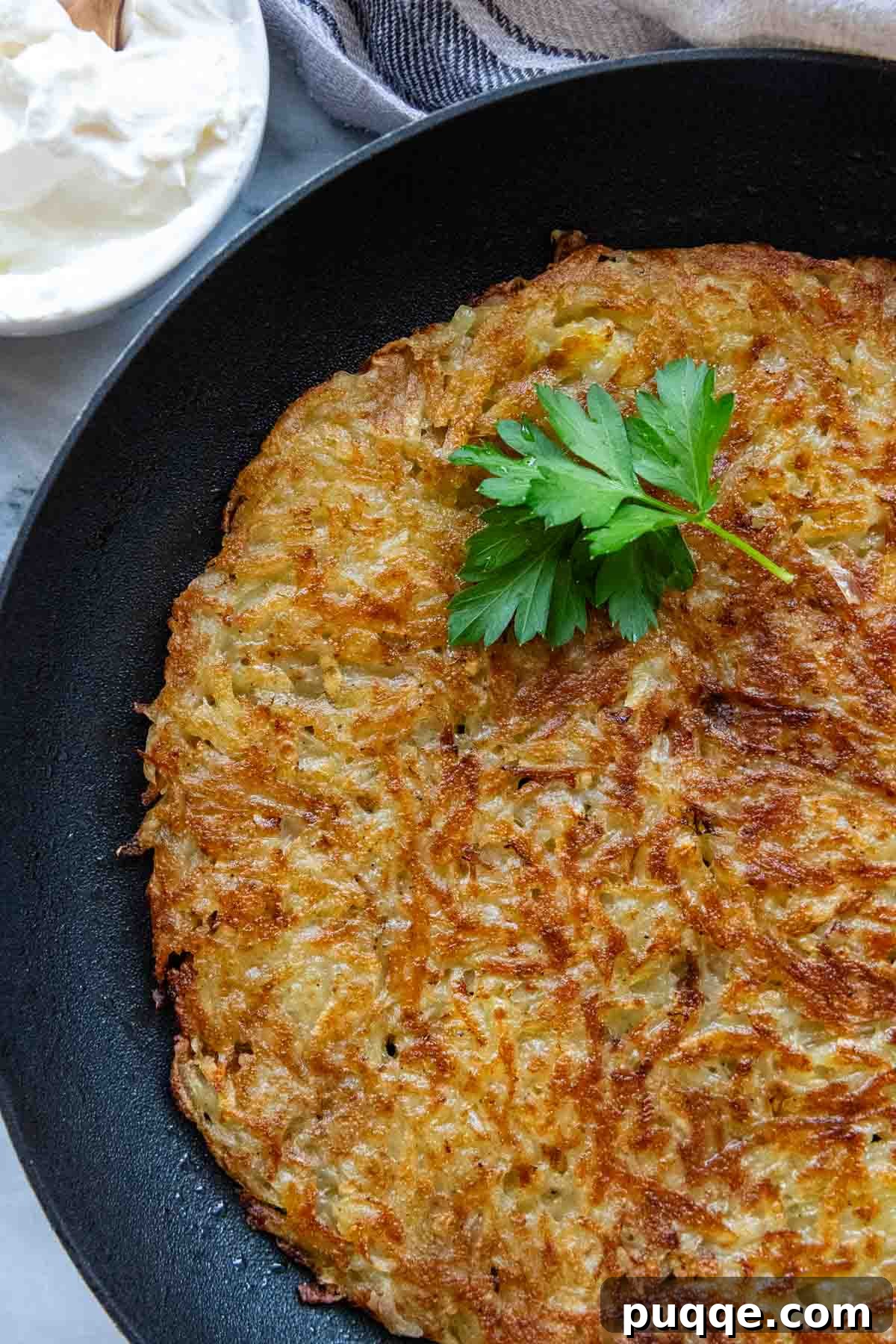 Effortless Crispy Potato Rösti 8 Golden-brown Swiss potato rosti cooling in a non-stick skillet, garnished with fresh green parsley.