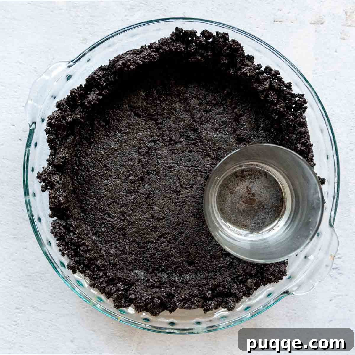 Easy Gluten-Free Oreo Crust for Perfect Slices 4 crust being pressed into a glass pie dish with a drinking glass.