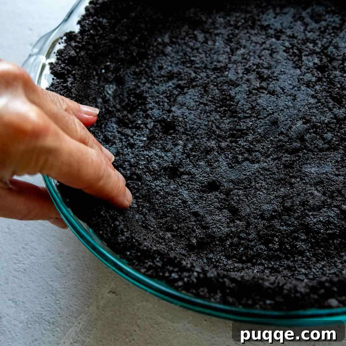 Easy Gluten-Free Oreo Crust for Perfect Slices 6 Side of oreo crust being pressed up the side of a glass pie dish by hands.