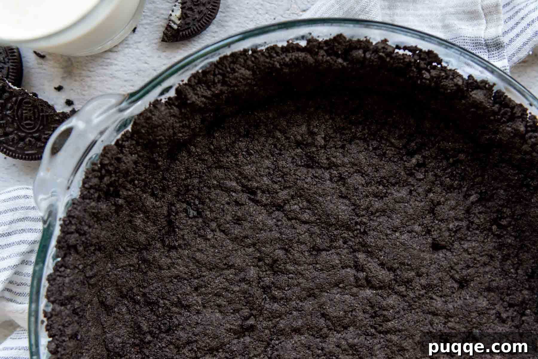 Easy Gluten-Free Oreo Crust for Perfect Slices 9 overhead close-up the baked pie crust in a glass pie dish with milk and cookies next to it.