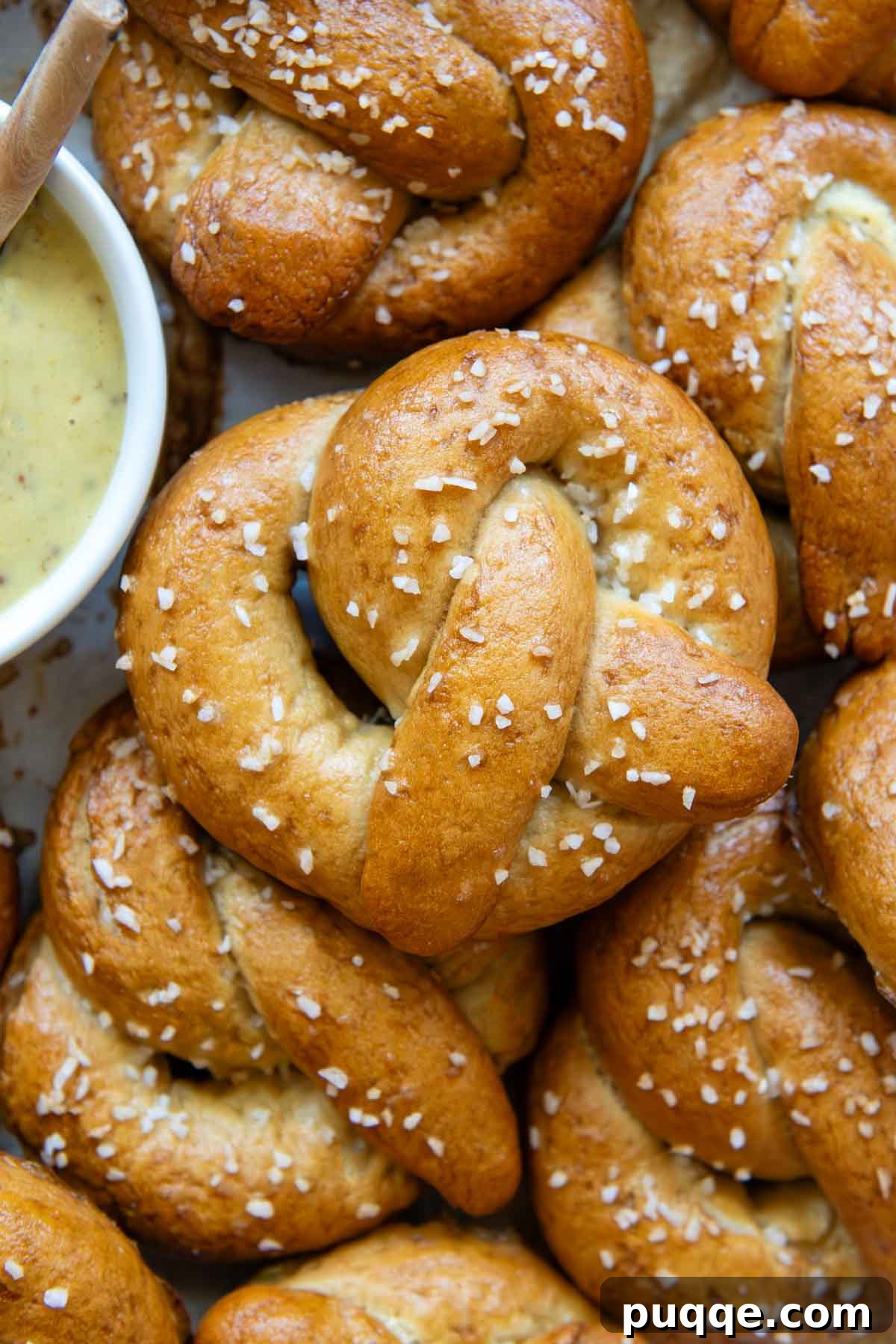 Pillowy Soft Gluten-Free Pretzels Simple Recipe 2 Close up overhead view of a perfectly golden brown gluten-free pretzel, sprinkled with white salt flakes, with a bowl of savory mustard dipping sauce to the left.