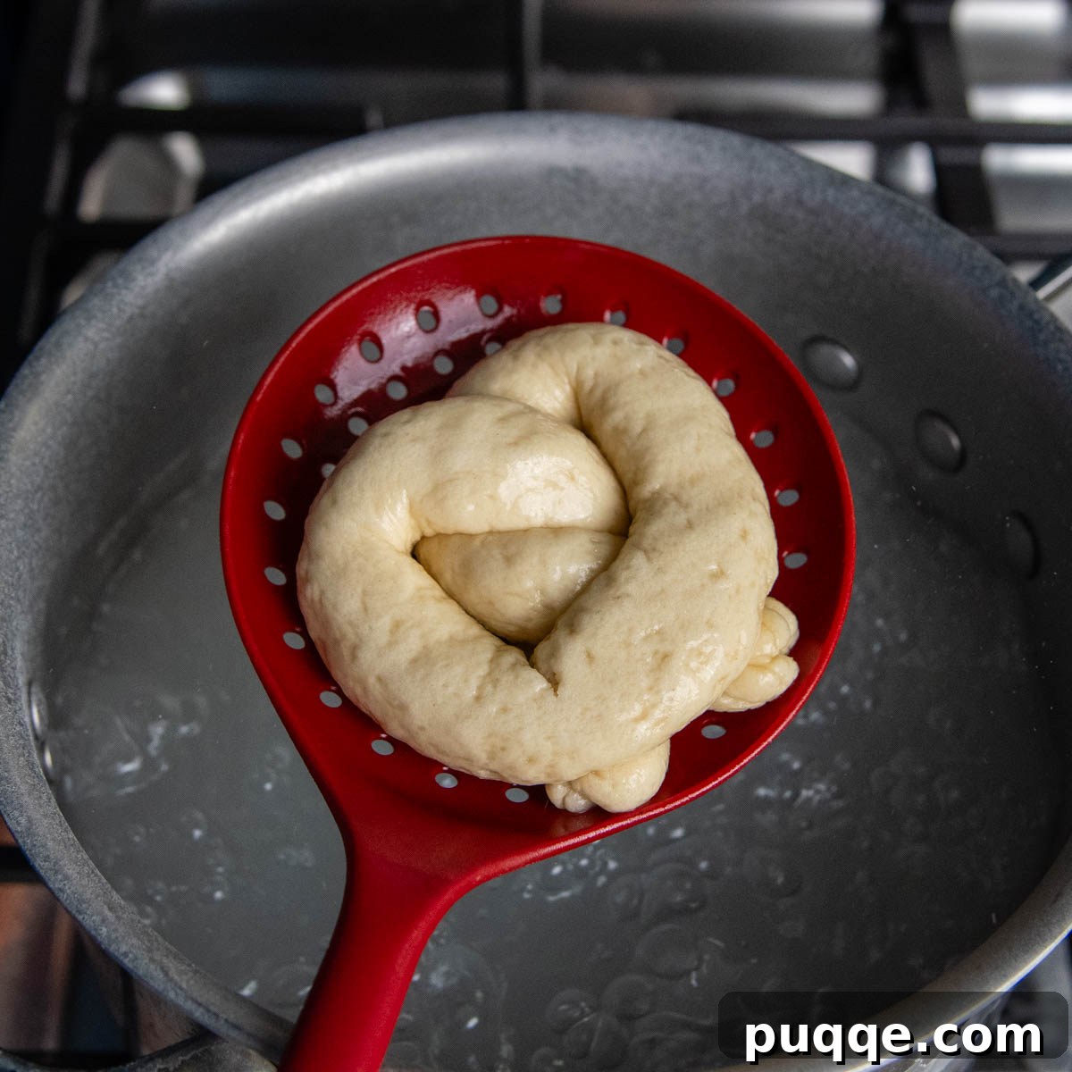 Pillowy Soft Gluten-Free Pretzels Simple Recipe 12 A fully shaped gluten-free pretzel being held in a slotted spoon, gently lowered into a pot of boiling water.