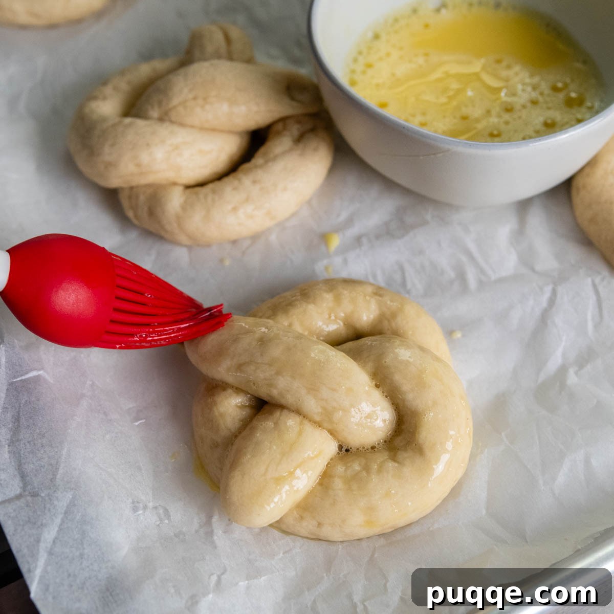 Pillowy Soft Gluten-Free Pretzels Simple Recipe 13 A boiled gluten-free pretzel resting on parchment paper, being brushed with an egg wash.
