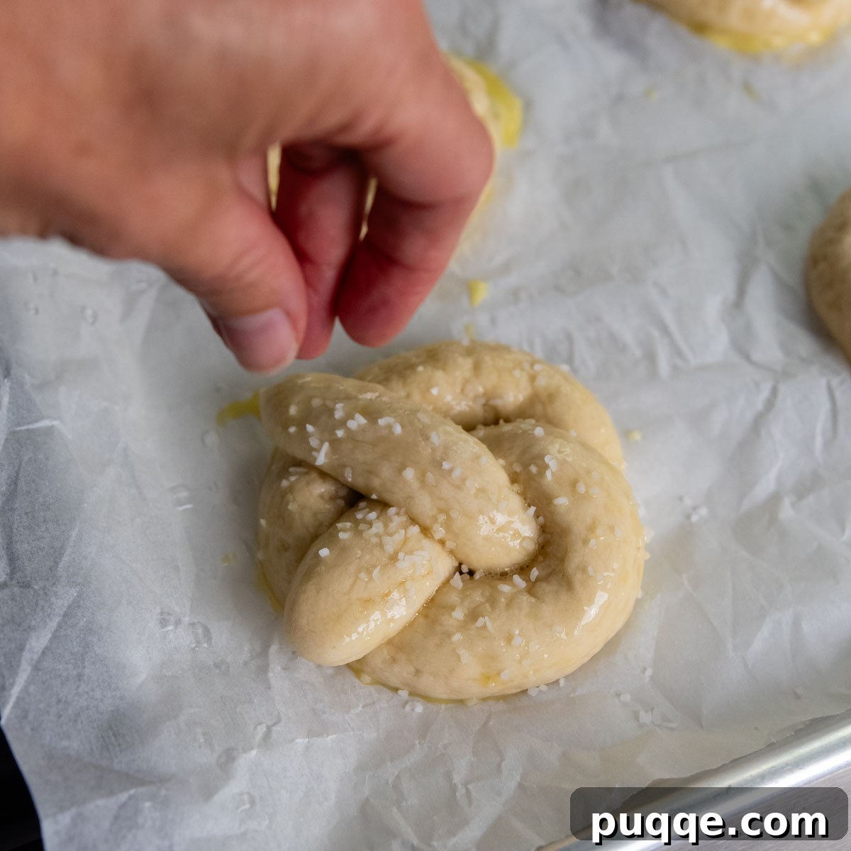Pillowy Soft Gluten-Free Pretzels Simple Recipe 14 A hand sprinkling coarse salt onto an unbaked, egg-washed gluten-free pretzel.