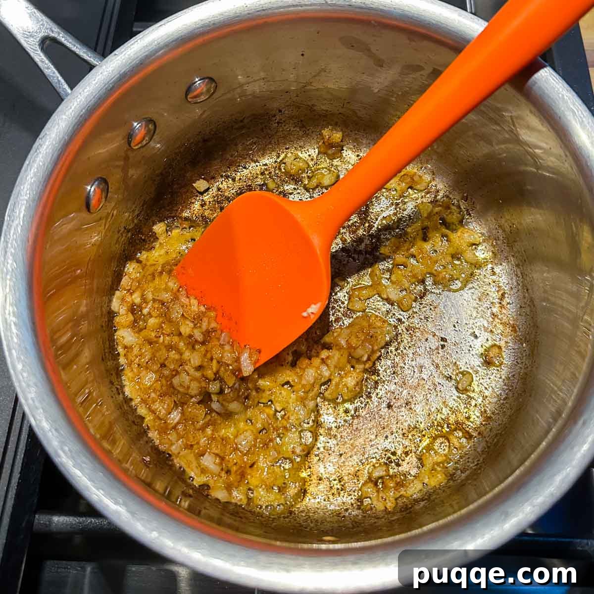 Diced onions being sautéed and browned in melted butter within a saucepan, creating a fragrant base.