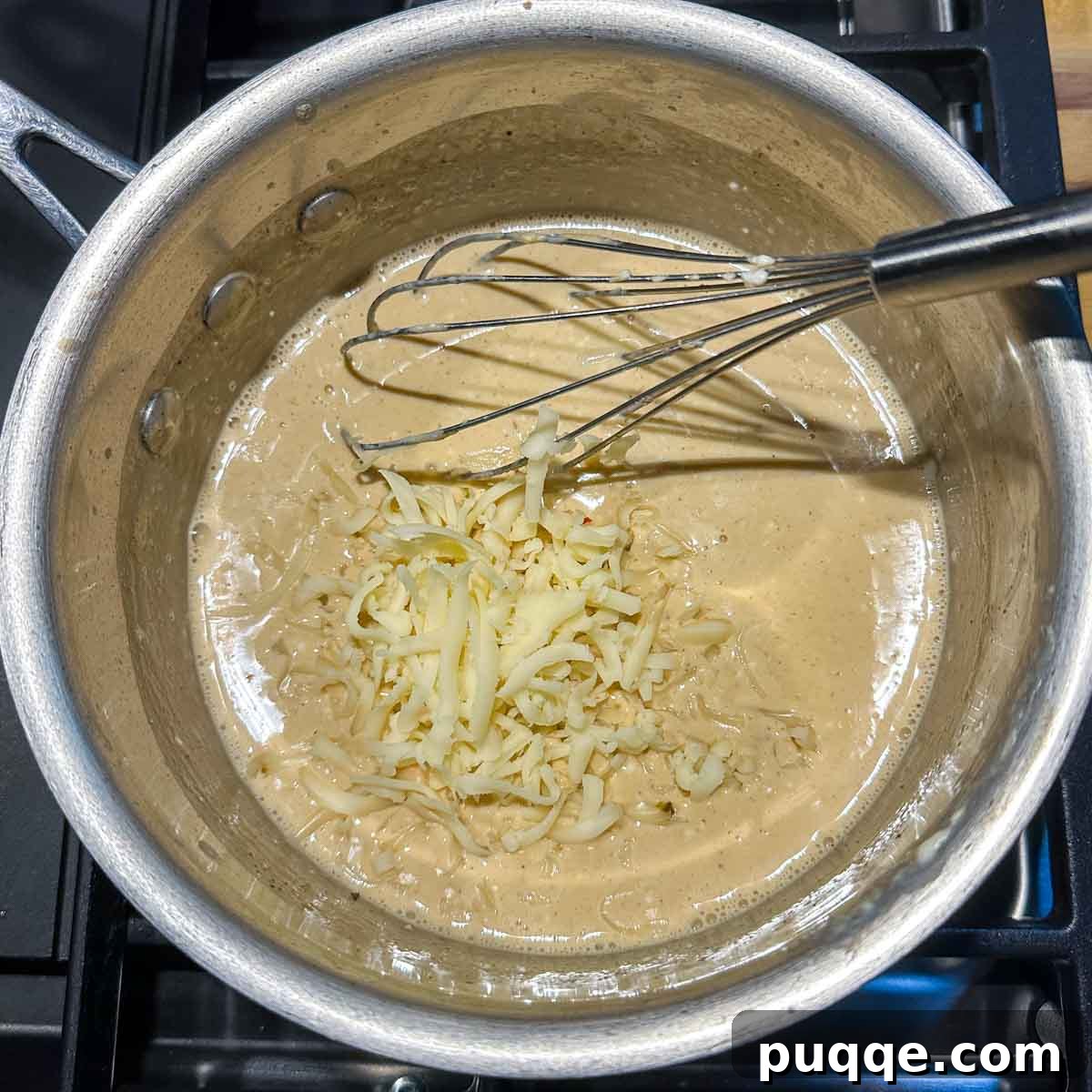 Freshly grated cheese being steadily added to the simmering liquid base in a saucepan, ready to be whisked into a smooth queso.