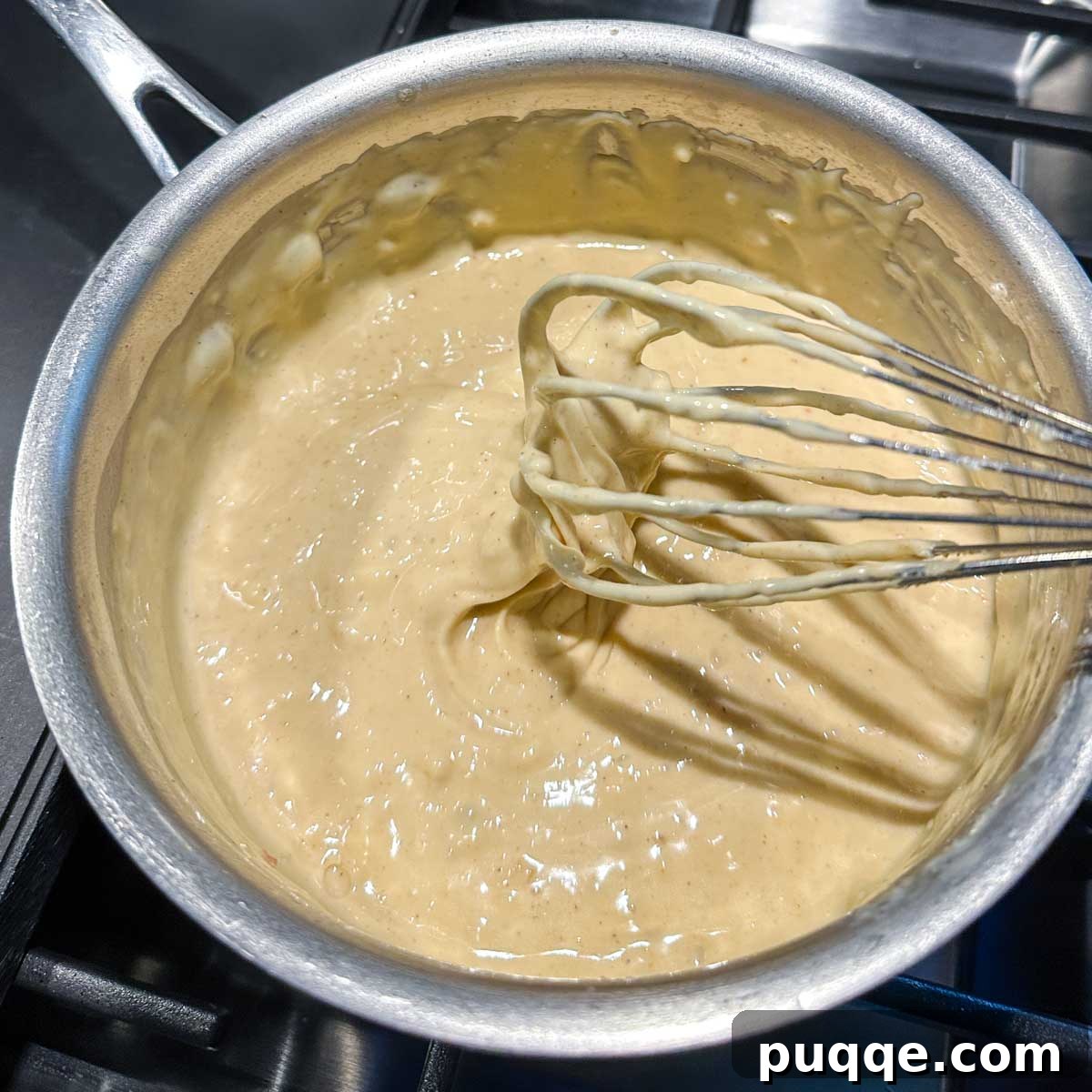 A whisk being lifted from the fully melted and smooth cheese sauce, demonstrating its luscious, thick consistency.
