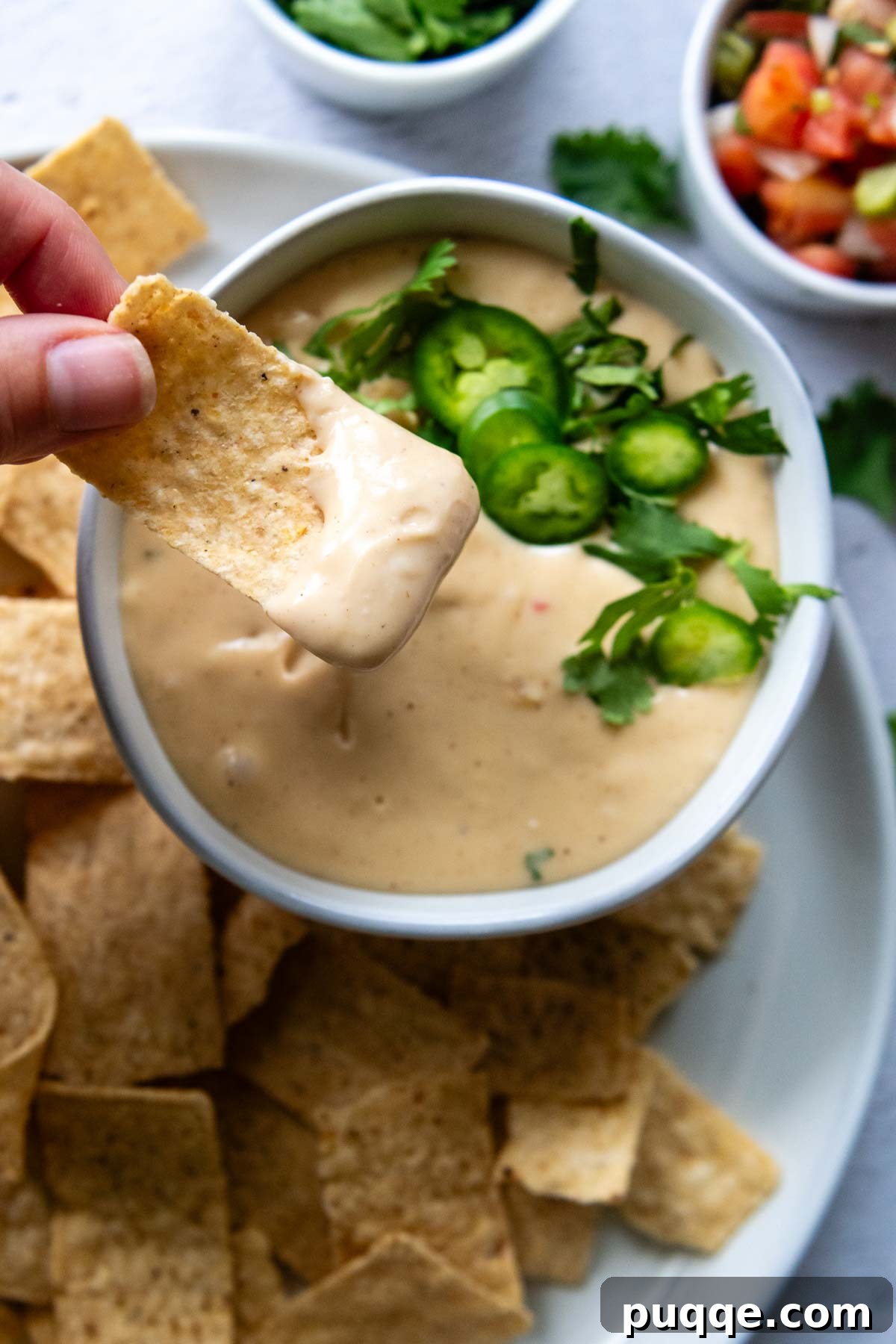 A hand dipping a crispy tortilla chip into a bowl of creamy, zesty gluten-free queso cheese sauce.