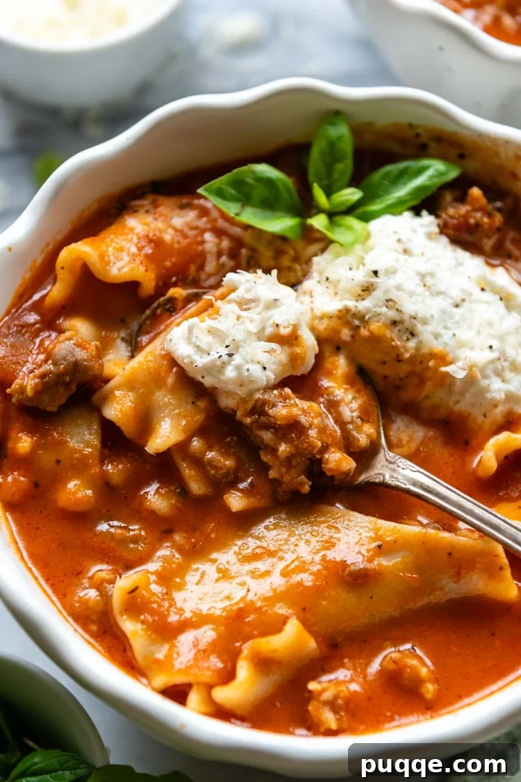 Ultimate 30-Minute Gluten-Free Lasagna Soup 2 A steaming bowl of Gluten-Free Lasagna Soup, garnished with fresh basil leaves and a dollop of creamy ricotta, is artfully displayed in a white bowl. A spoon rests beside it, inviting you to dig in.