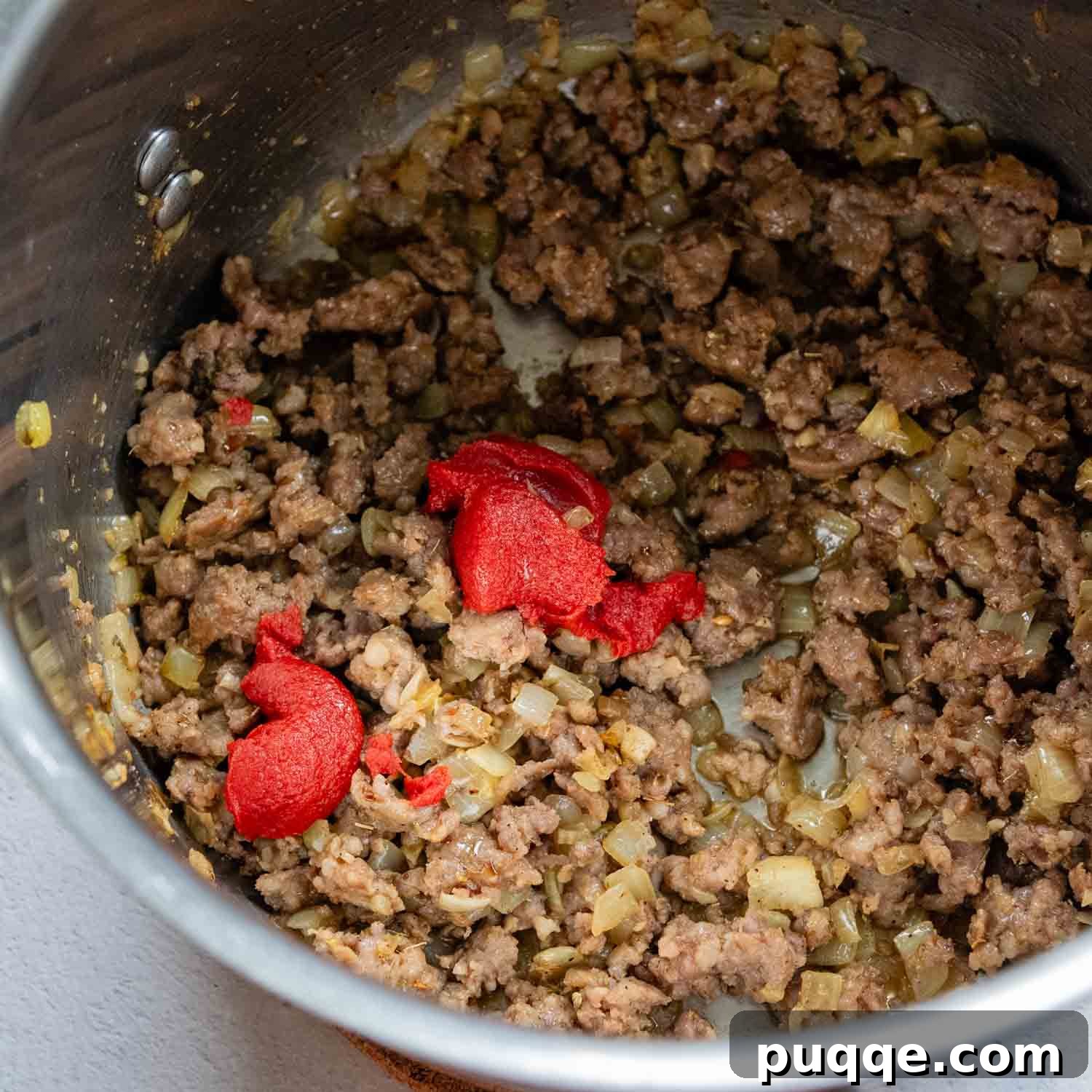 Ultimate 30-Minute Gluten-Free Lasagna Soup 3 A pot on the stove filled with cooked Italian sausage and a dollop of rich tomato paste, ready to be stirred in.