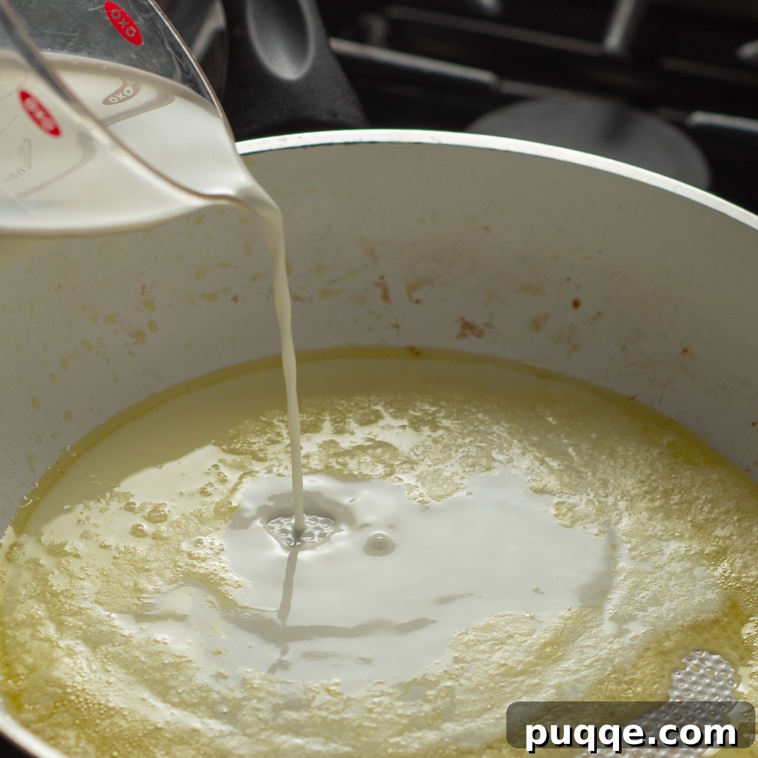 Creamy half and half being poured into a skillet with pesto and other sauce ingredients.