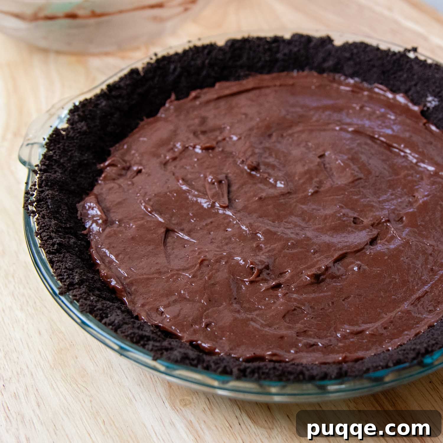 A thick, creamy layer of chocolate pudding evenly spread over the baked Oreo crust in a glass pie dish, forming the second layer of the dessert.