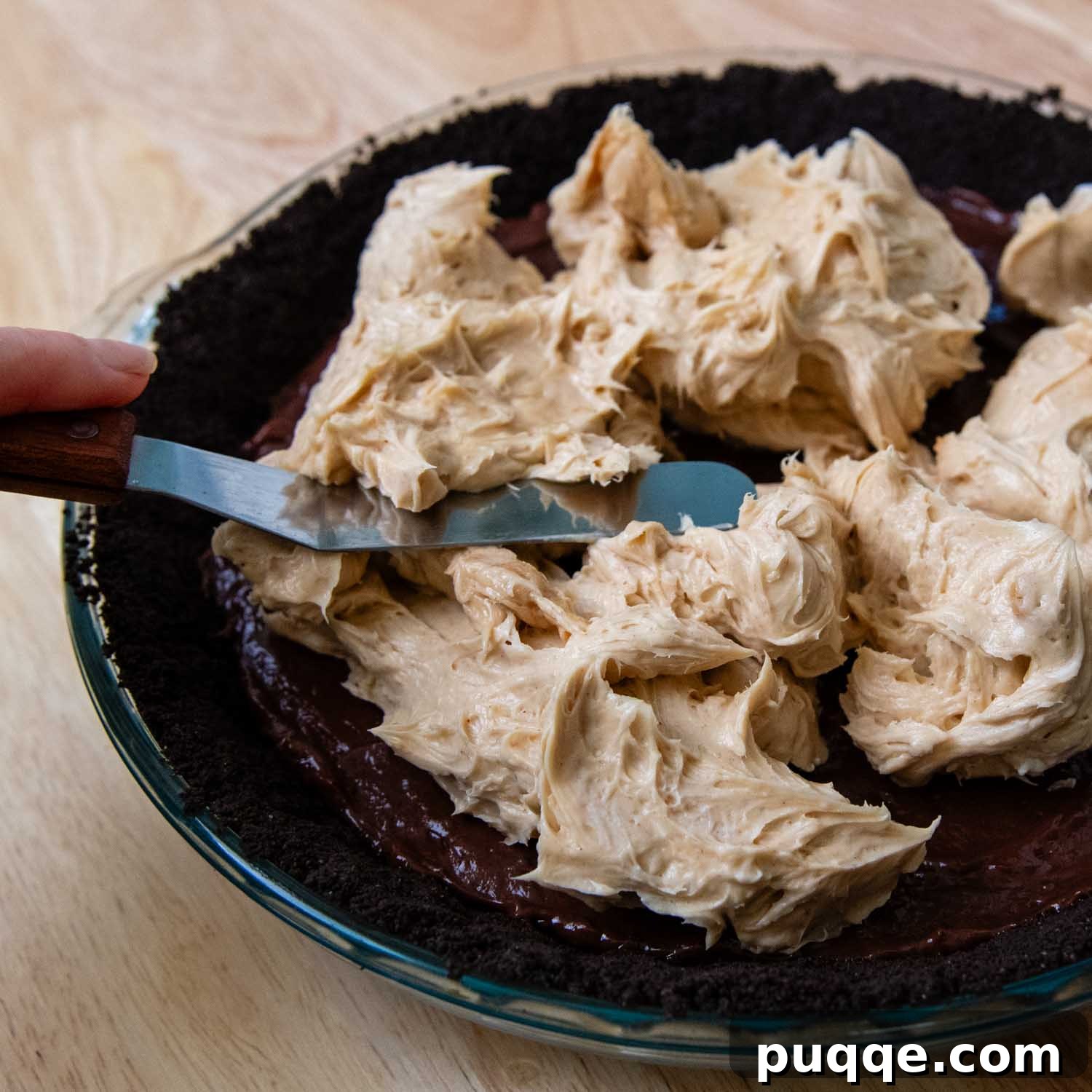 A fluffy, creamy peanut butter mixture being spread smoothly over the chocolate pudding layer in a pie dish, creating the delectable third layer of the pie.