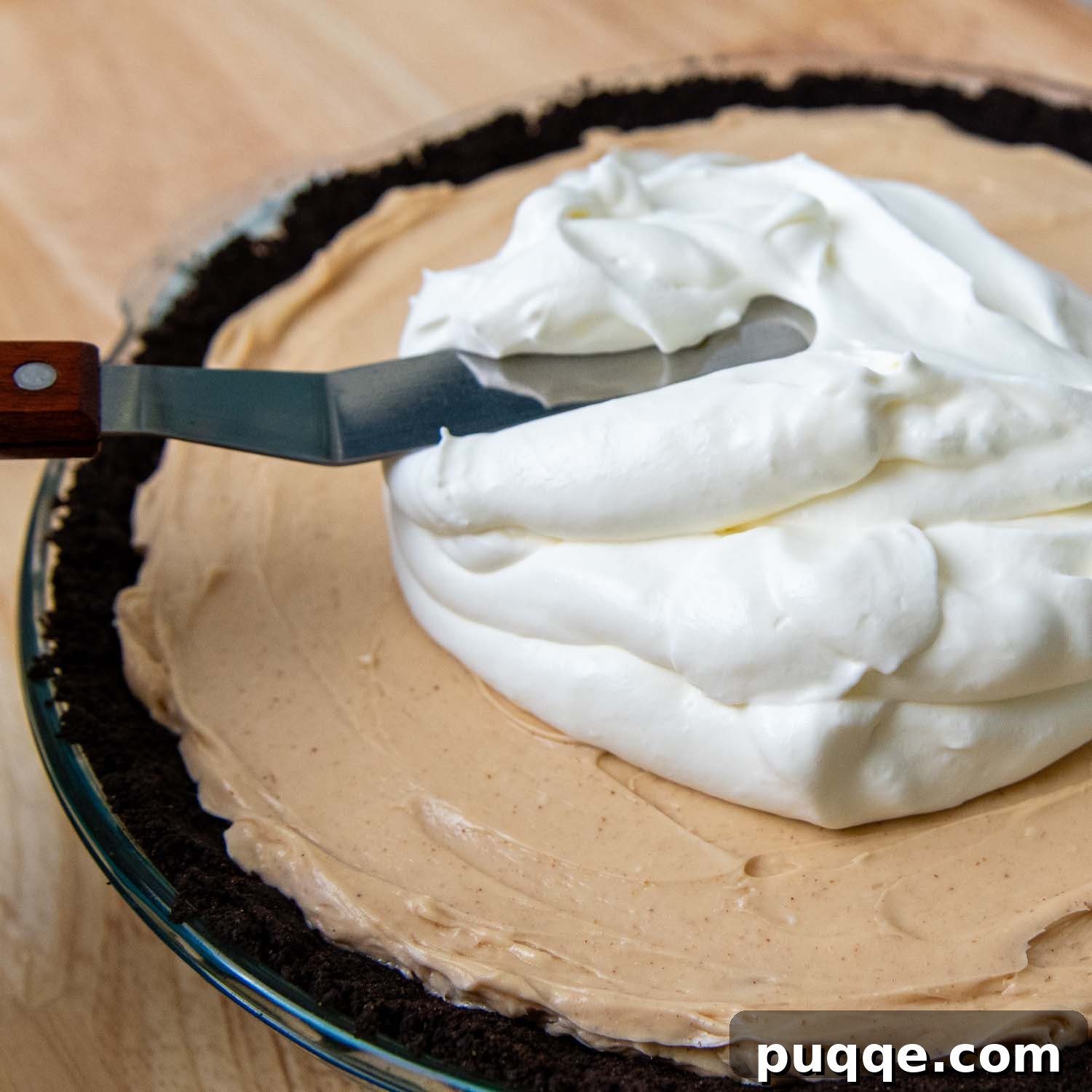 A luscious layer of whipped topping being gently spread over the peanut butter filling, creating a smooth, airy crown for the pie before the final drizzle.