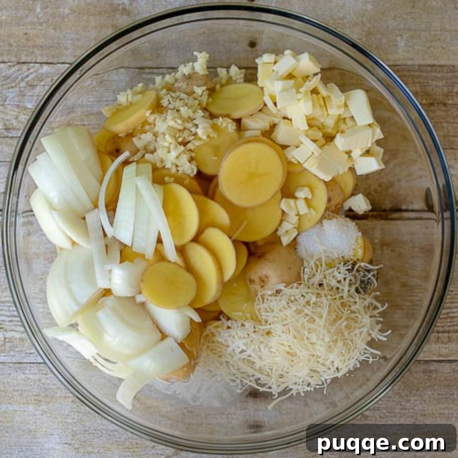All the ingredients for grilled potatoes, including sliced potatoes, onions, garlic, butter, cream, and parmesan, in a large mixing bowl, ready to be tossed.