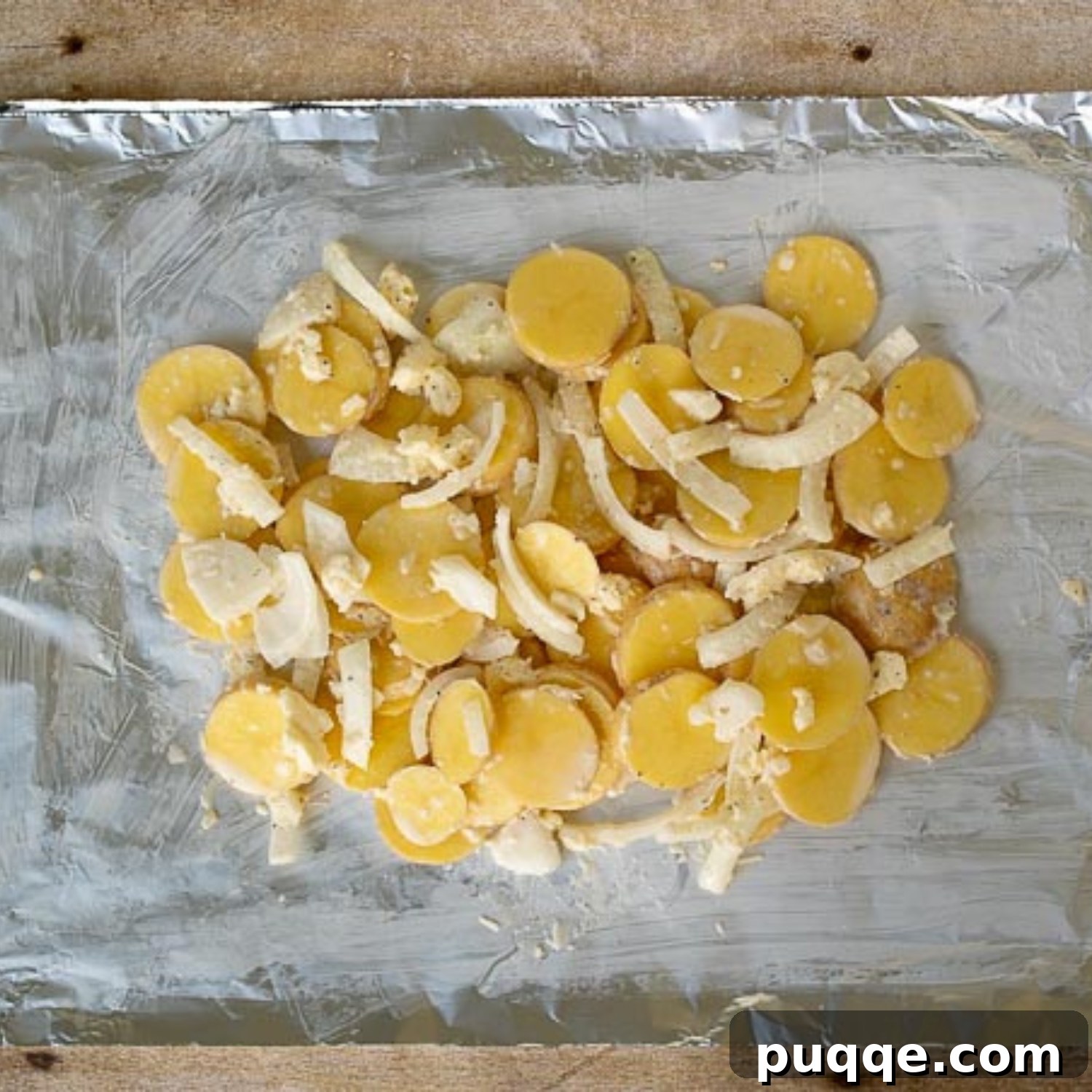 Thinly sliced potatoes and onions spread onto a buttered sheet of foil, ready for sealing into a packet.