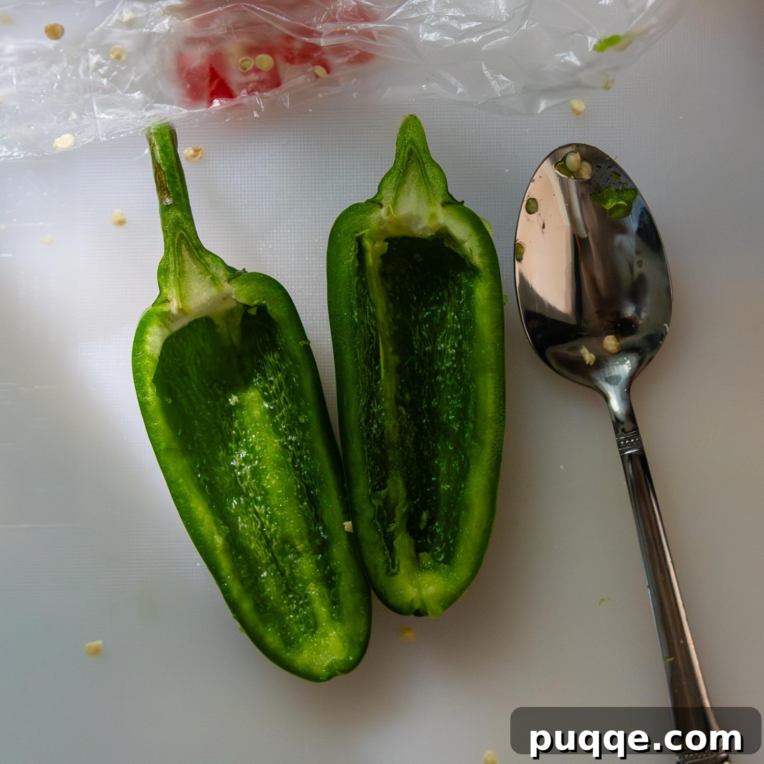Crispy Baked Gluten-Free Jalapeño Poppers (Grain-Free) 4 A cleaned jalapeño half with seeds and membrane removed, placed on a cutting board next to a spoon, demonstrating the scraping process.