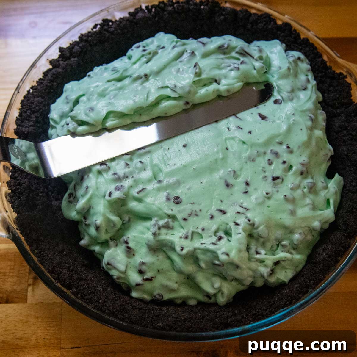 No Bake Chocolate Mint Dream Pie 6 The creamy mint filling being spread smoothly over the chocolate Oreo crust in a pie plate, a step towards assembling the delicious dessert.
