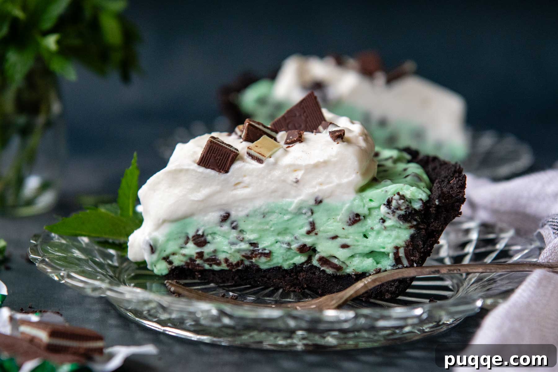 No Bake Chocolate Mint Dream Pie 8 A side view of a delightful Andes mint pie on a glass plate, with a fork gently pulling away a piece, clearly showing the three distinct layers: the dark chocolate crust, the vibrant green mint filling, and the white fluffy whipped topping.