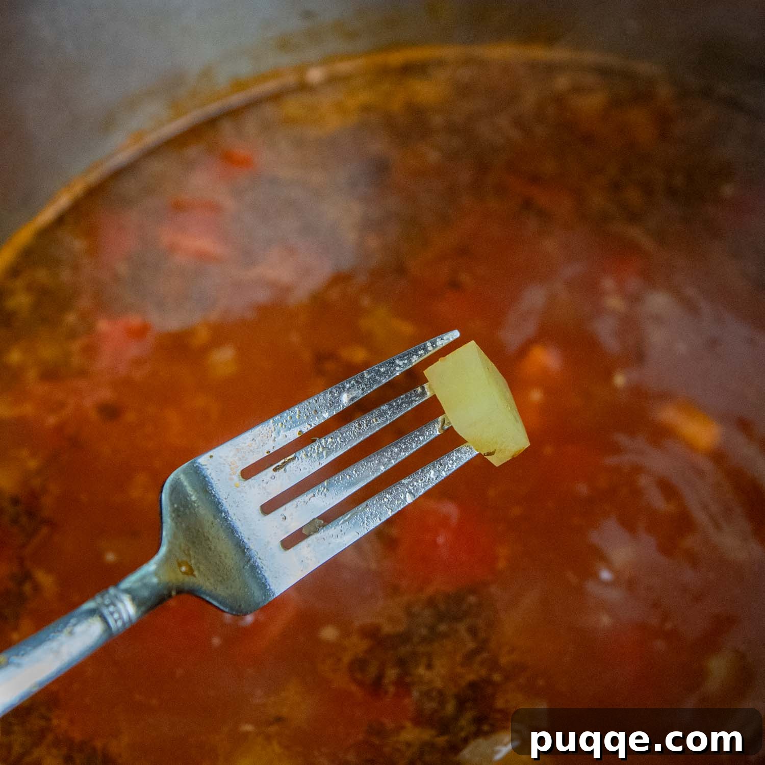 A fork lifting a tender potato from a simmering pot of vegetable soup, demonstrating perfect doneness.