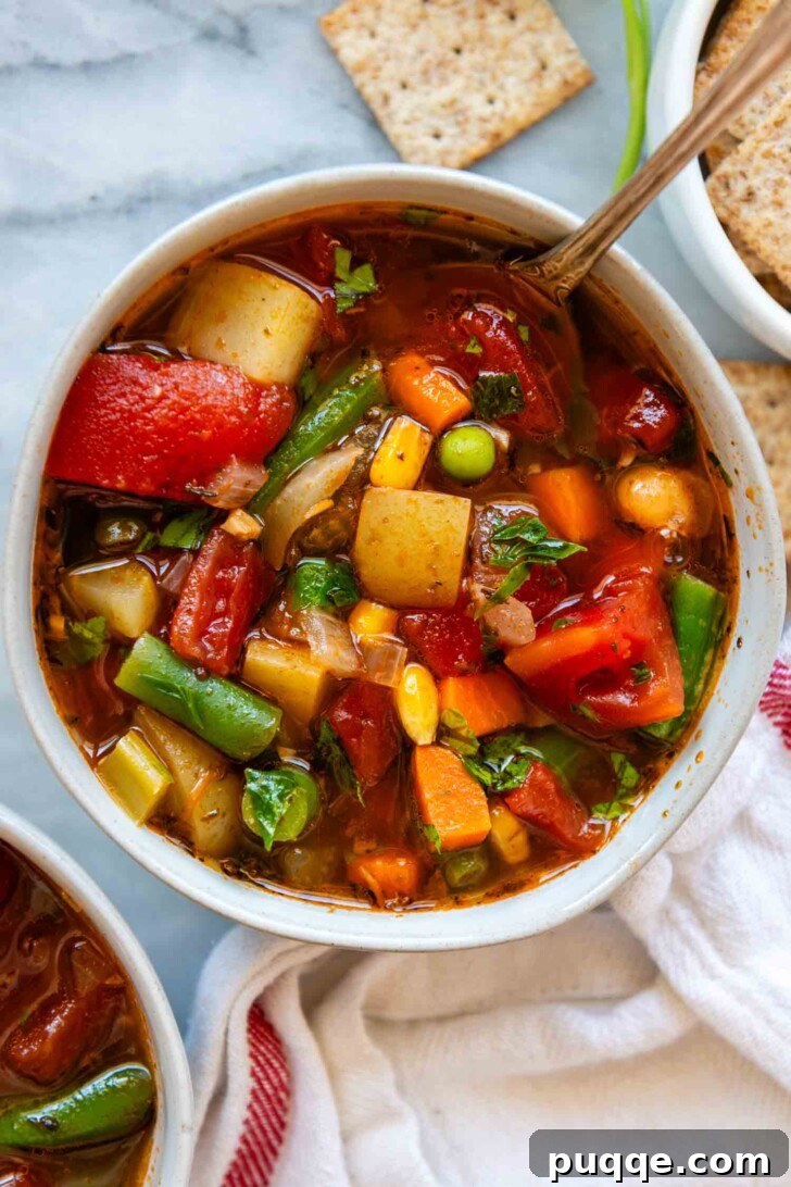 An overhead shot of a white bowl filled with vibrant, chunky vegetable soup, garnished with fresh parsley.