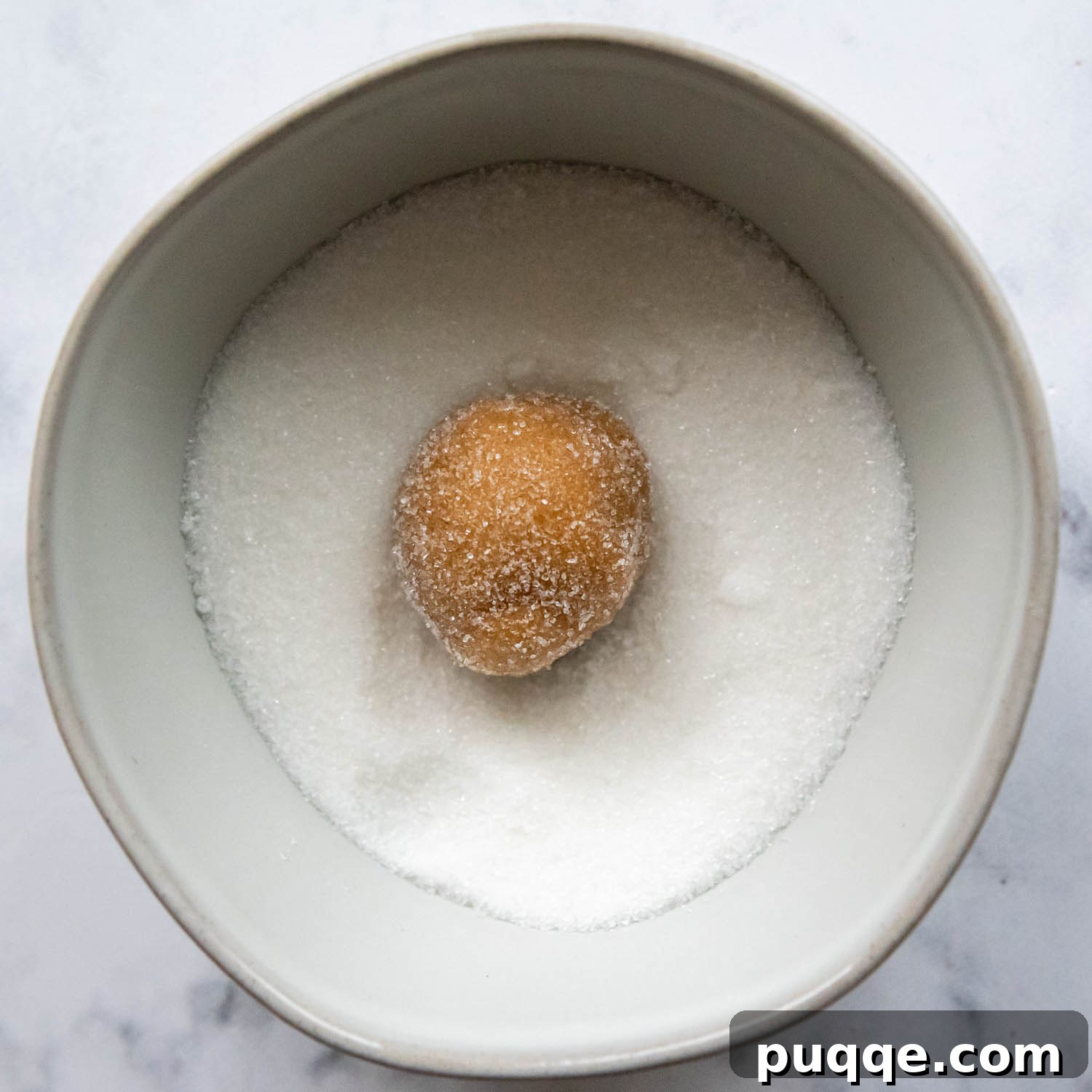 Old-Fashioned Tender Gluten-Free Peanut Butter Blossoms 6 A cookie ball in a bowl of sugar.