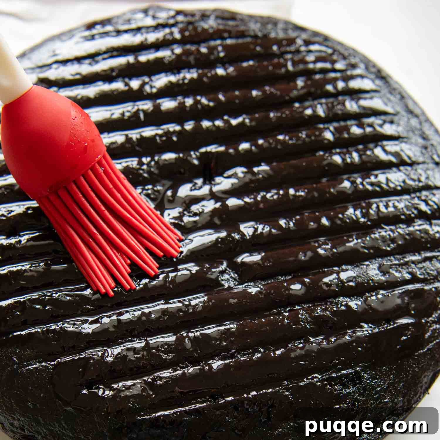 Cherry syrup being carefully brushed onto a baked chocolate cake layer, demonstrating the soaking process.