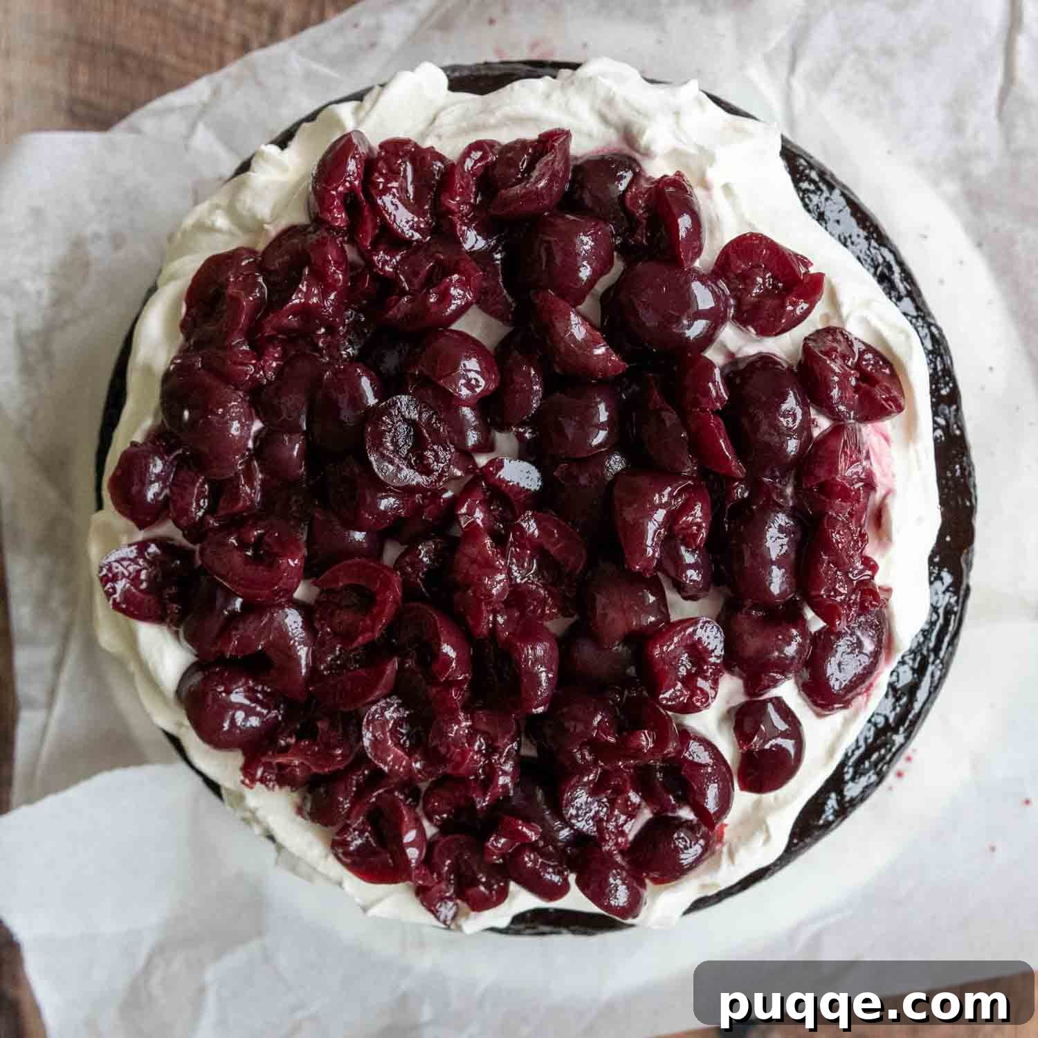 Overhead shot of halved cherries arranged on top of a whipped cream layer, ready for the next cake layer.