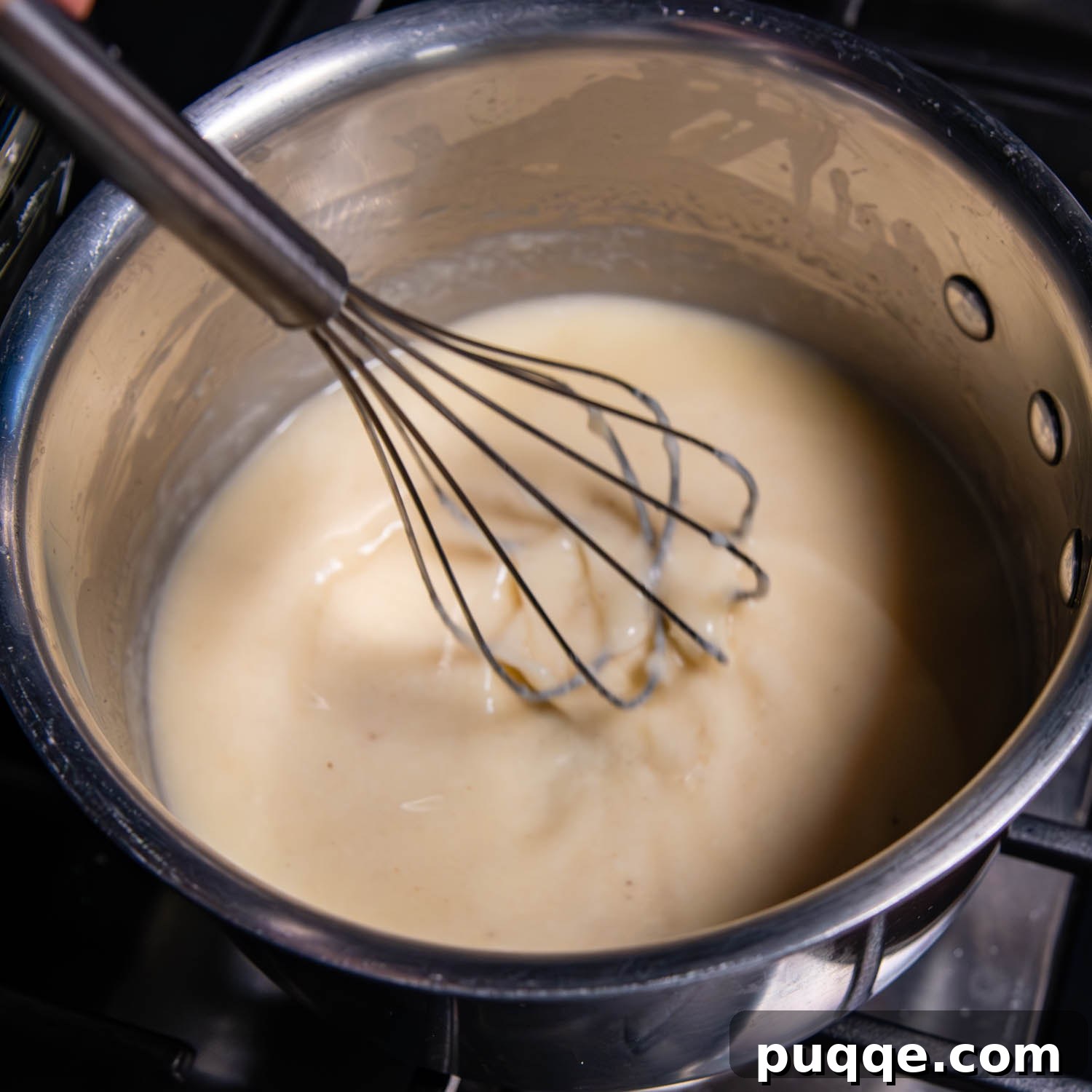 Effortless Creamy Gluten-Free Cheese Fondue 4 A stainless steel whisk rests inside a saucepan, filled with gently simmering white wine. The edges of the wine show faint bubbles, indicating the ideal low heat needed before adding the cheese.