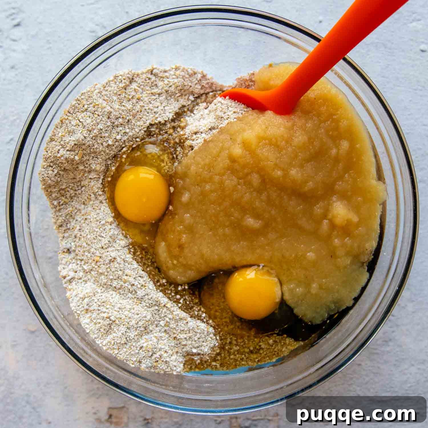 Wet and dry muffin ingredients in glass bowl with a red spatula, showcasing the combined batter.