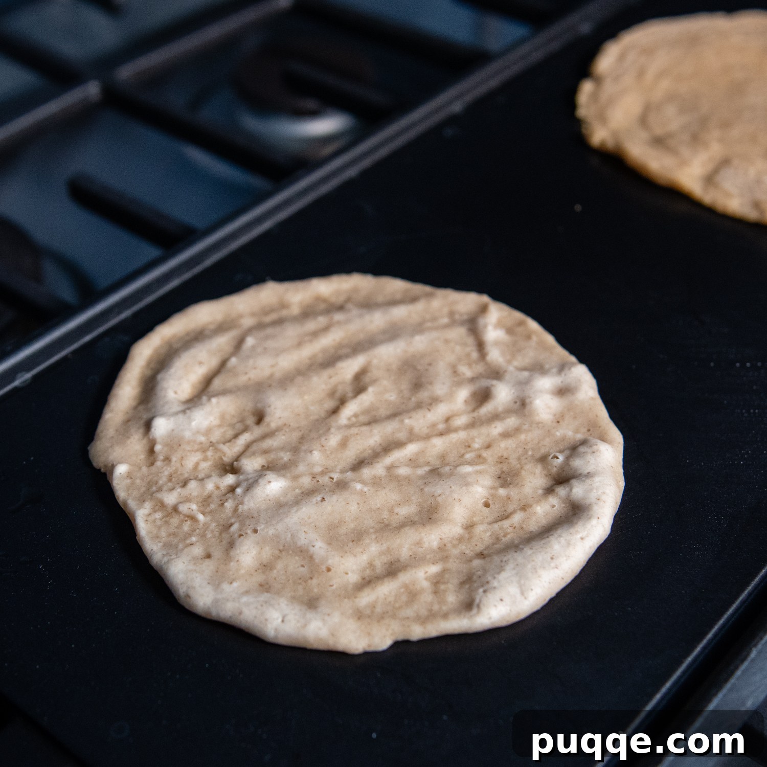 Effortlessly Soft and Pliable Oat Tortillas 7 Tortilla mix thinly spread into a uniform circle on a griddle, showing the cooking process.