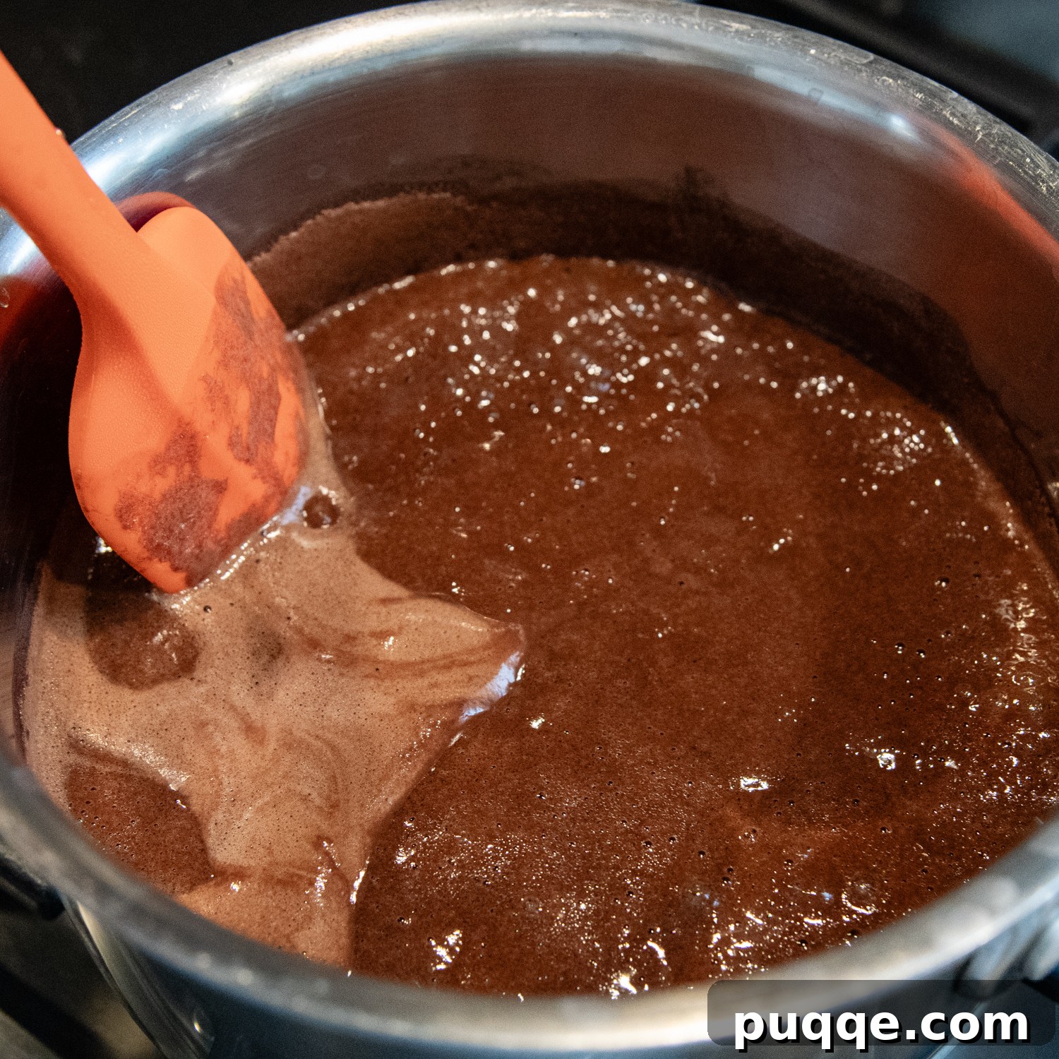 Cake ingredients, including a rich cocoa mixture, measured in a stainless steel bowl, ready to be combined with a spatula.