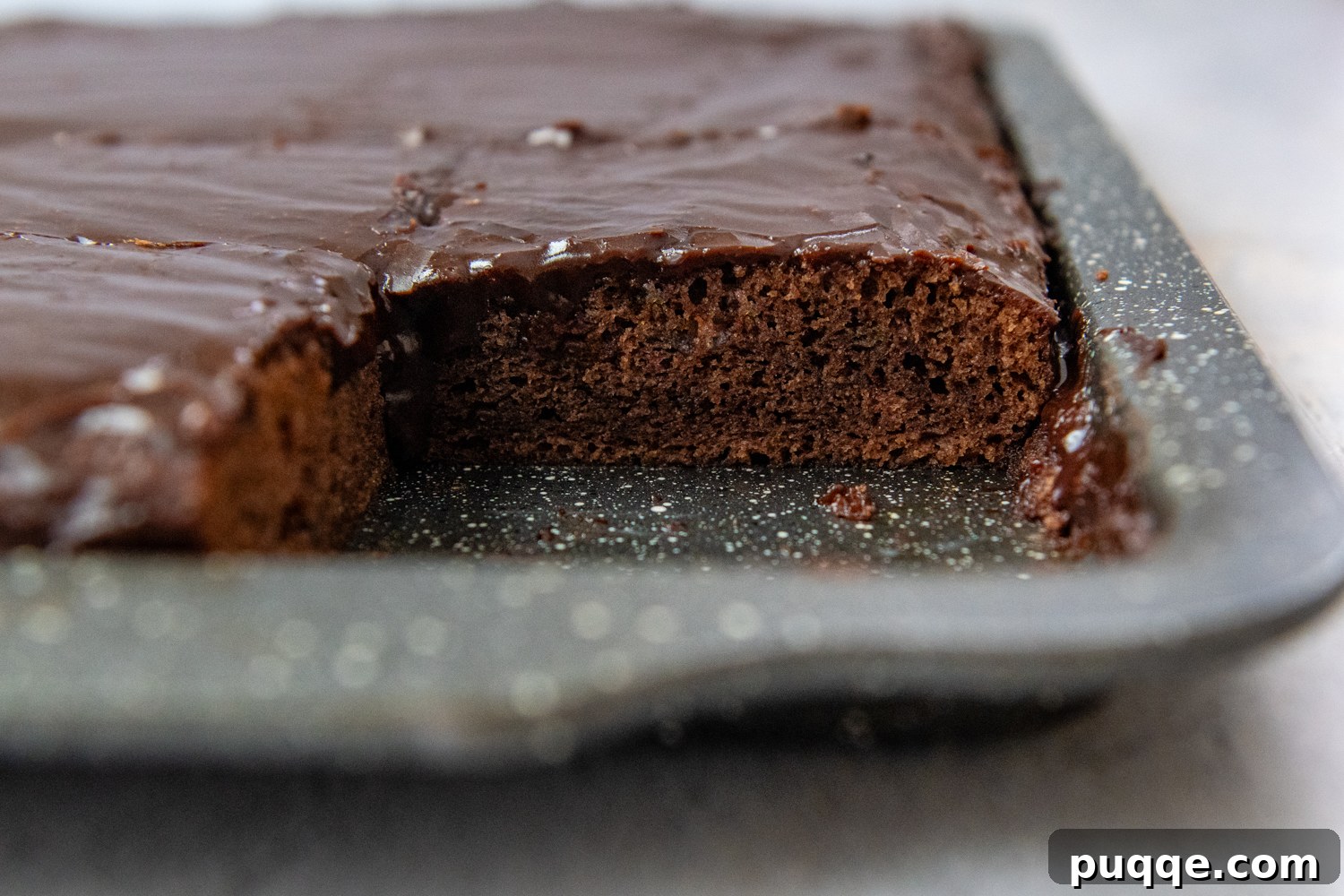 A freshly baked Gluten-Free Texas Sheet Cake still in the pan, with one slice perfectly removed, revealing its moist interior and luscious chocolate glaze.