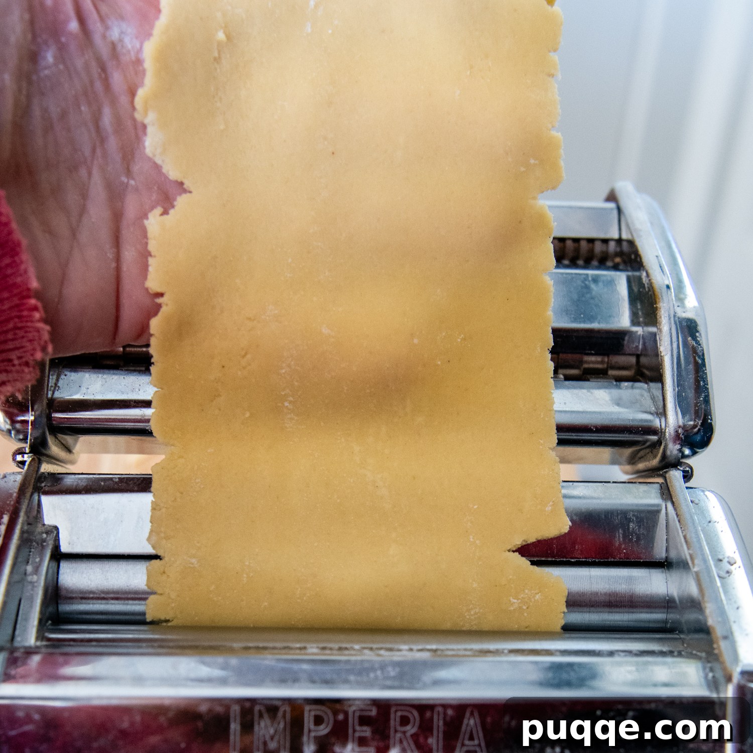 dough being flattened by pasta making machine.