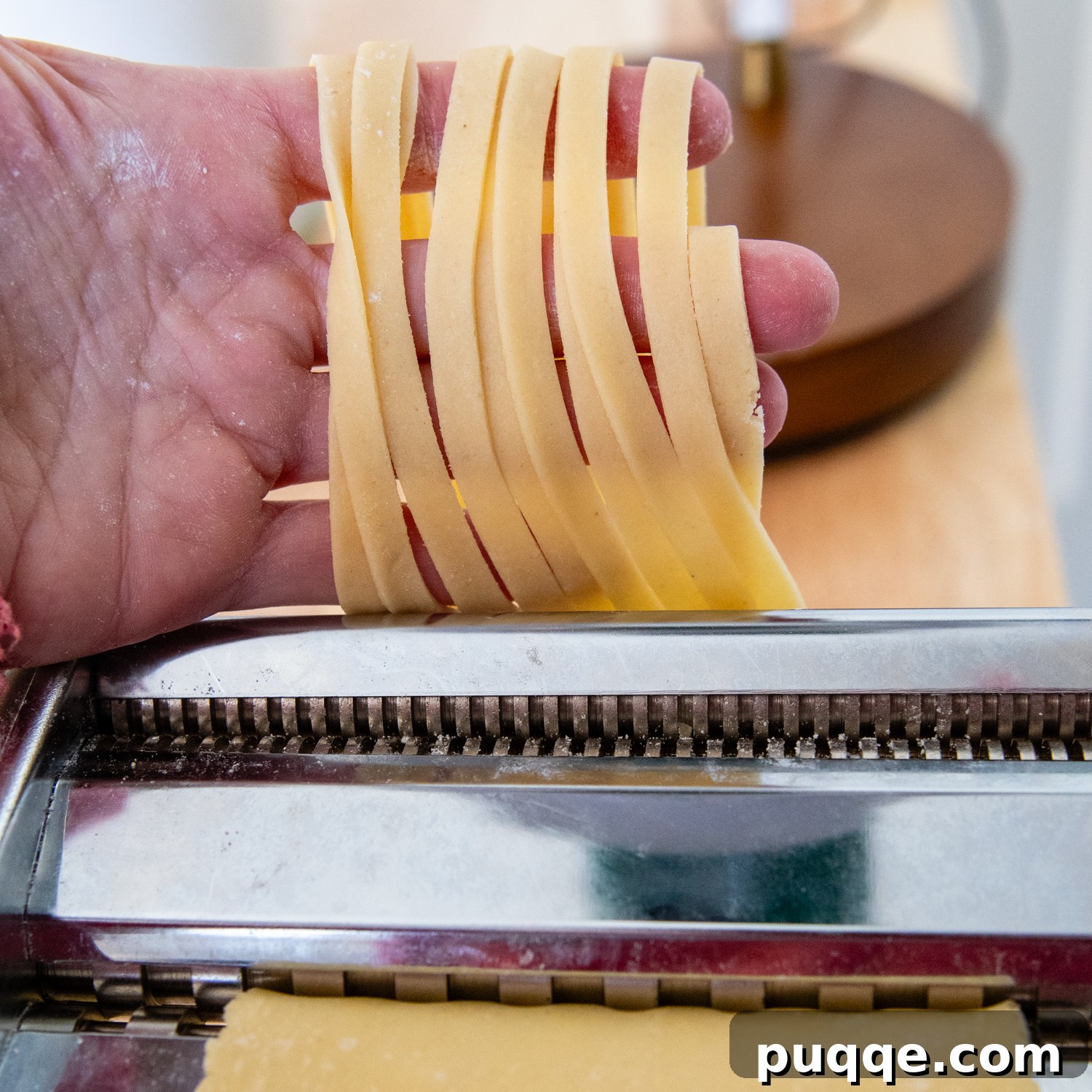 Dough coming out of a pasta maker in fettuccine shape.