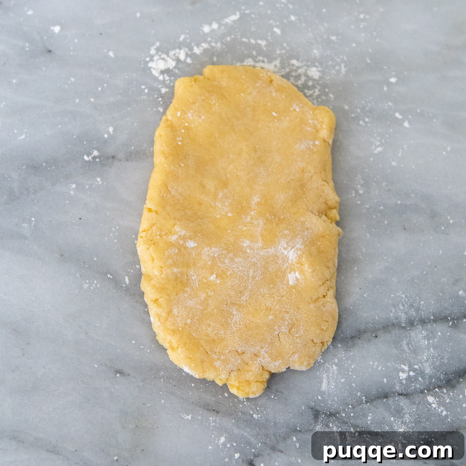 Pasta dough sprinkled with flour on a marble surface.