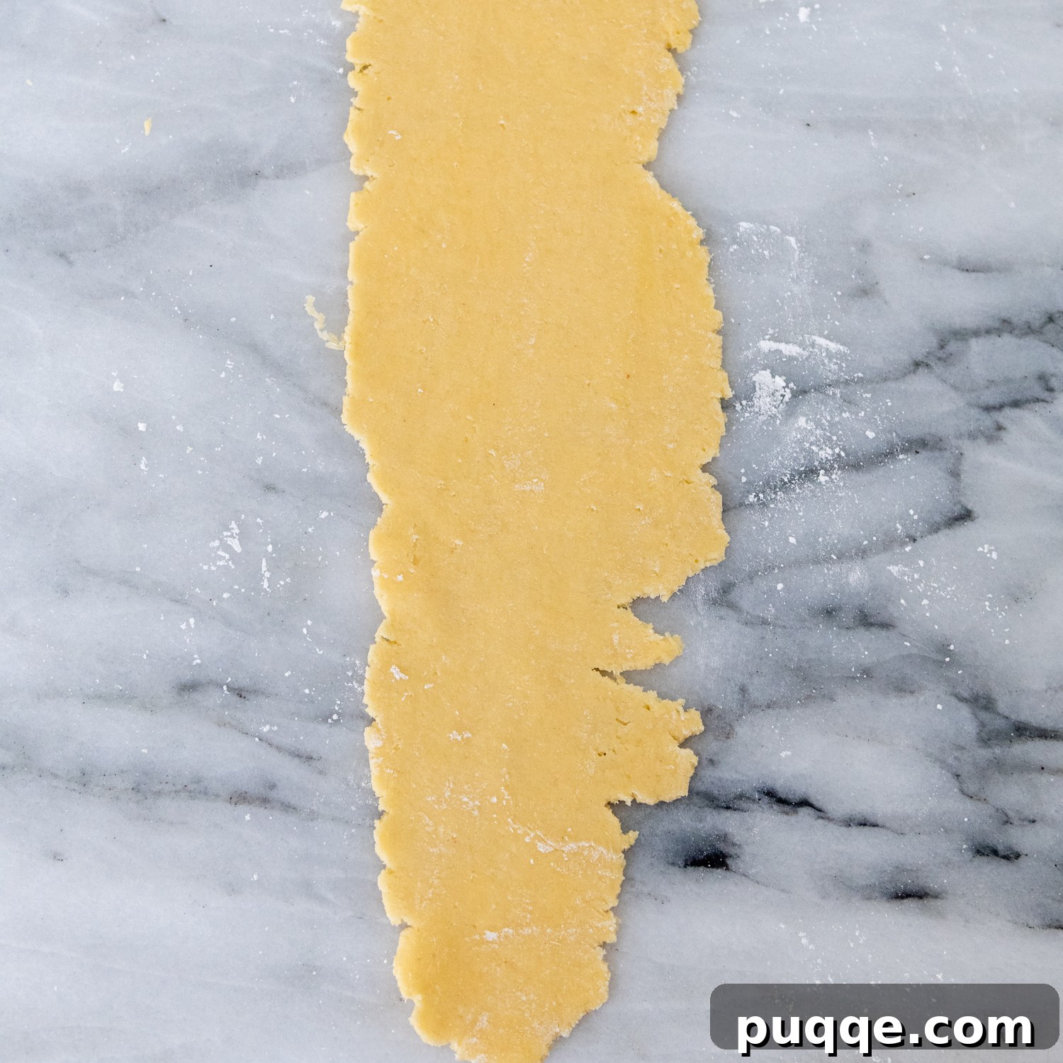 Dough flattened with ragged edges laying on a marble surface.