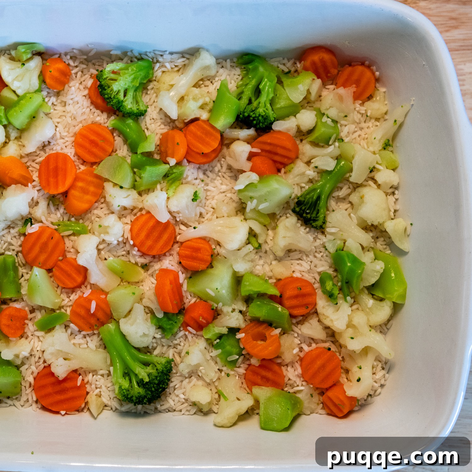 Wholesome & Creamy Gluten-Free Chicken Bake 3 Casserole ingredients including rice, frozen mixed vegetables, and raw seasoned chicken pieces neatly arranged in a white baking dish, ready for sauce.