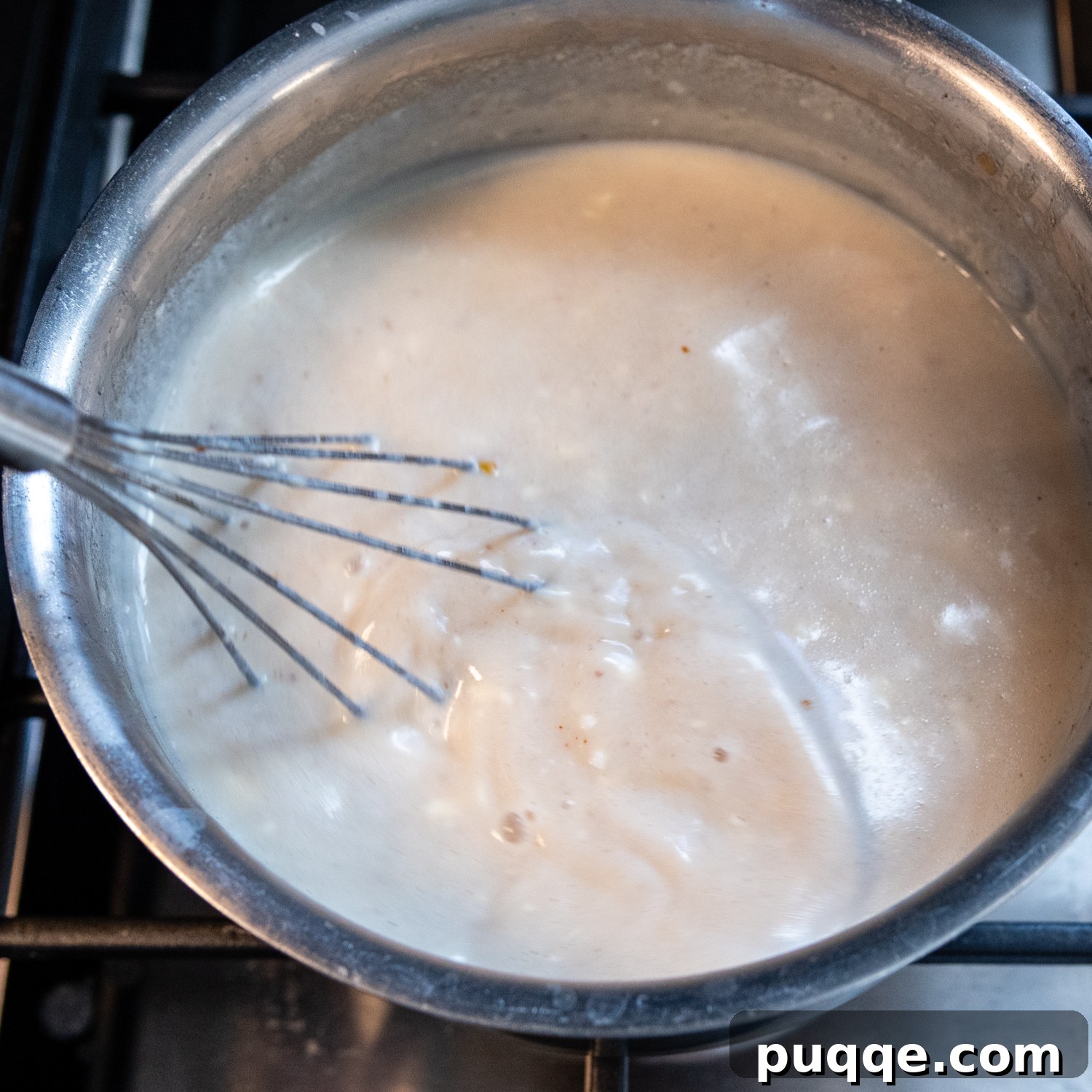 Wholesome & Creamy Gluten-Free Chicken Bake 6 A close-up of a flat whisk stirring a creamy, white cheese sauce in a saucepan.
