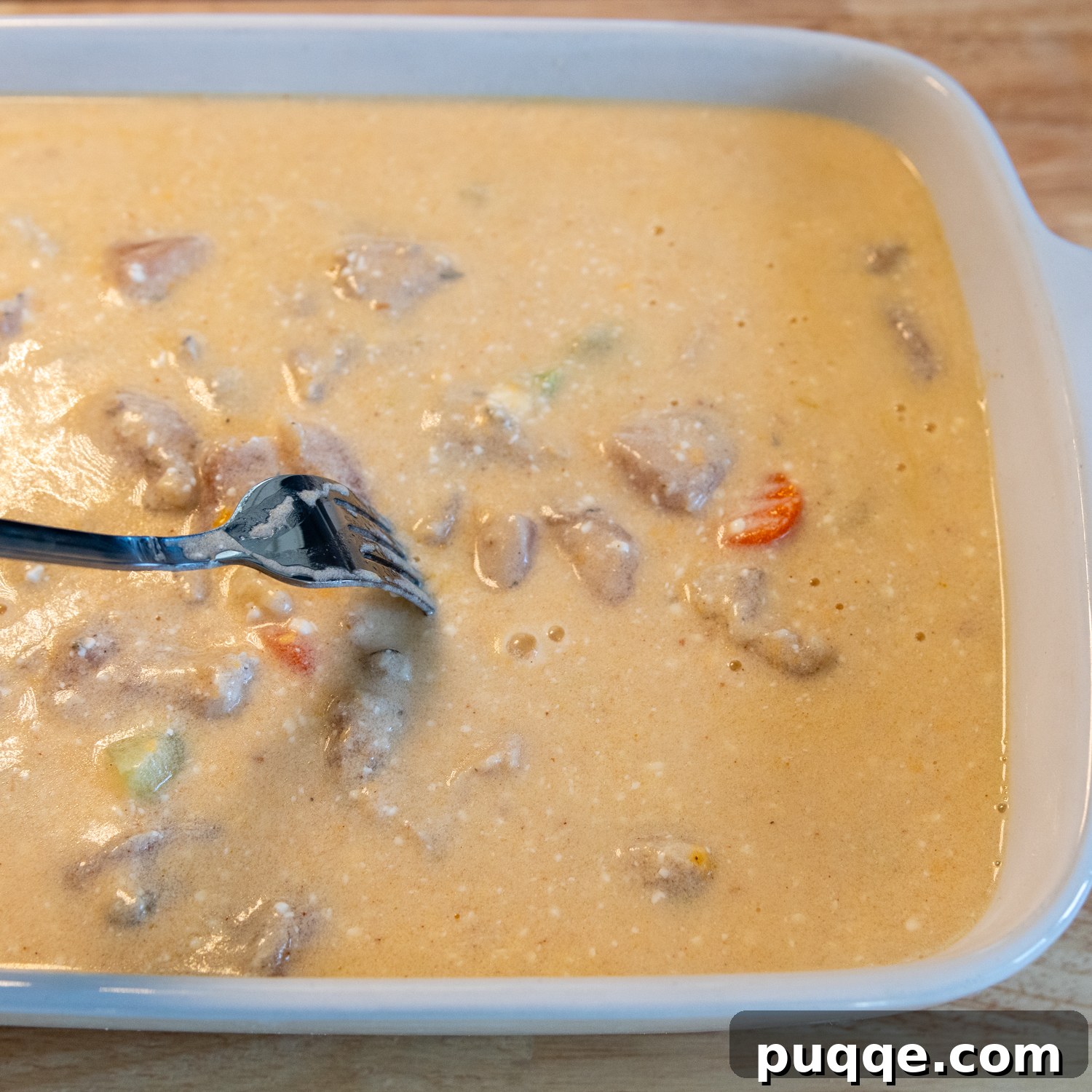 Wholesome & Creamy Gluten-Free Chicken Bake 7 A fork gently stirring the layers of rice, chicken, vegetables, and creamy sauce in a white baking dish before baking.