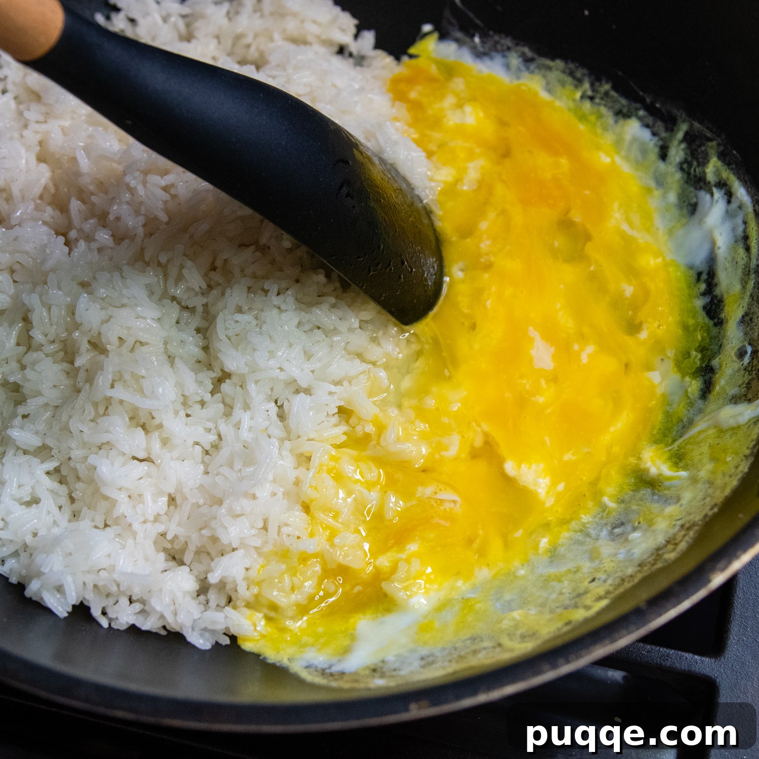 Quick Gluten-Free Fried Rice: Your Perfect Weeknight Meal 5 Scrambling eggs in a wok, pushed to one side, next to frying rice. A spoon is mixing the eggs.