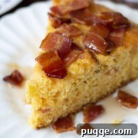 a wedge of bacon maple cornbread on a white plate with syrup drizzled over